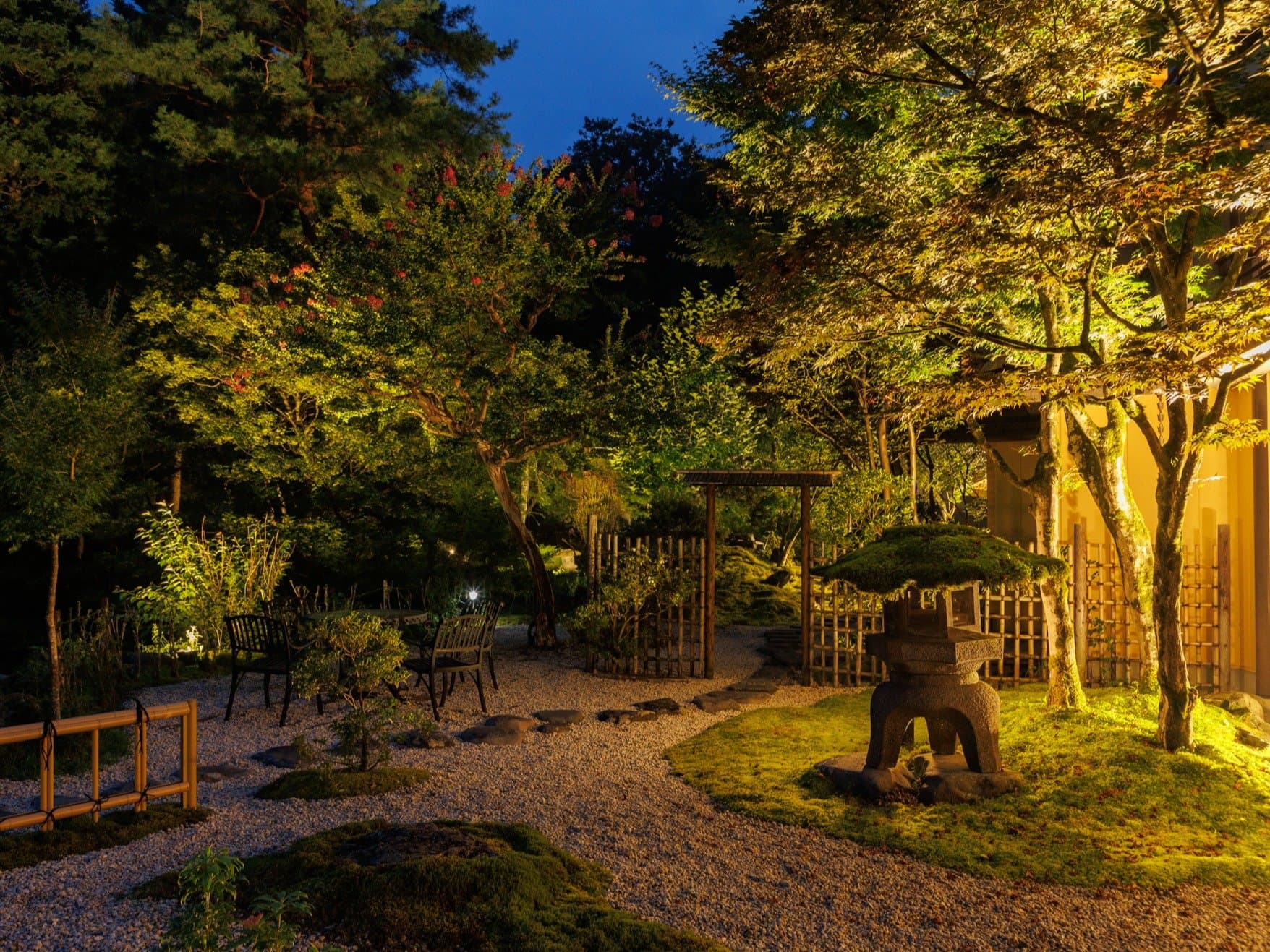 Illuminated Japanese garden at Nikko Hoshi no Yado at dusk with stone lantern, maples and a gravel path