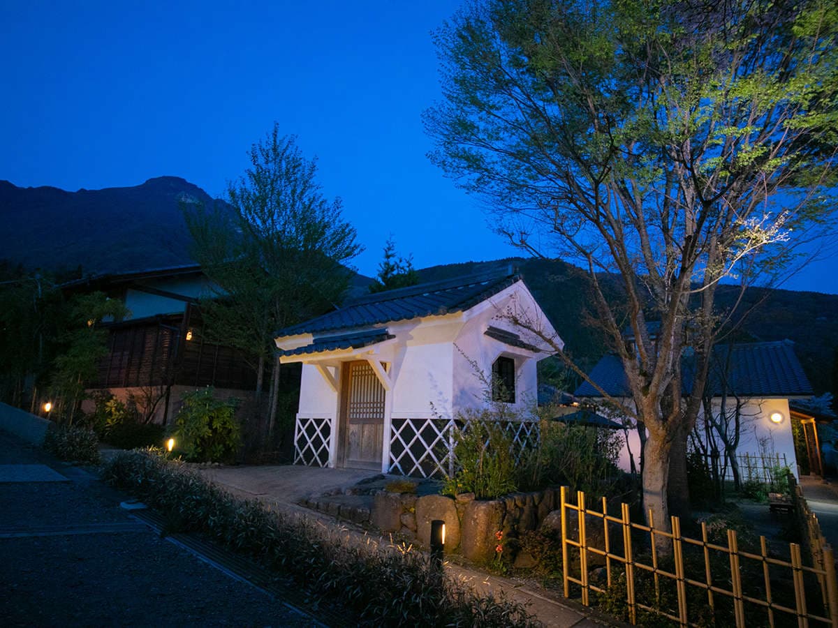 Oyado Ichizen ryokan exterior at blue-hour dusk with warm-lit windows in Yufuin Onsen