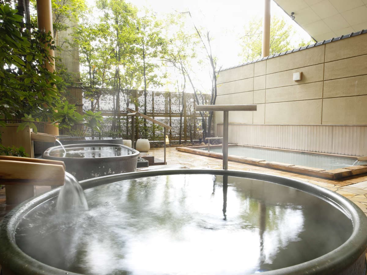 Round open-air hot-spring tub at Dogo Prince Hotel with rising steam and a paved garden bathing area