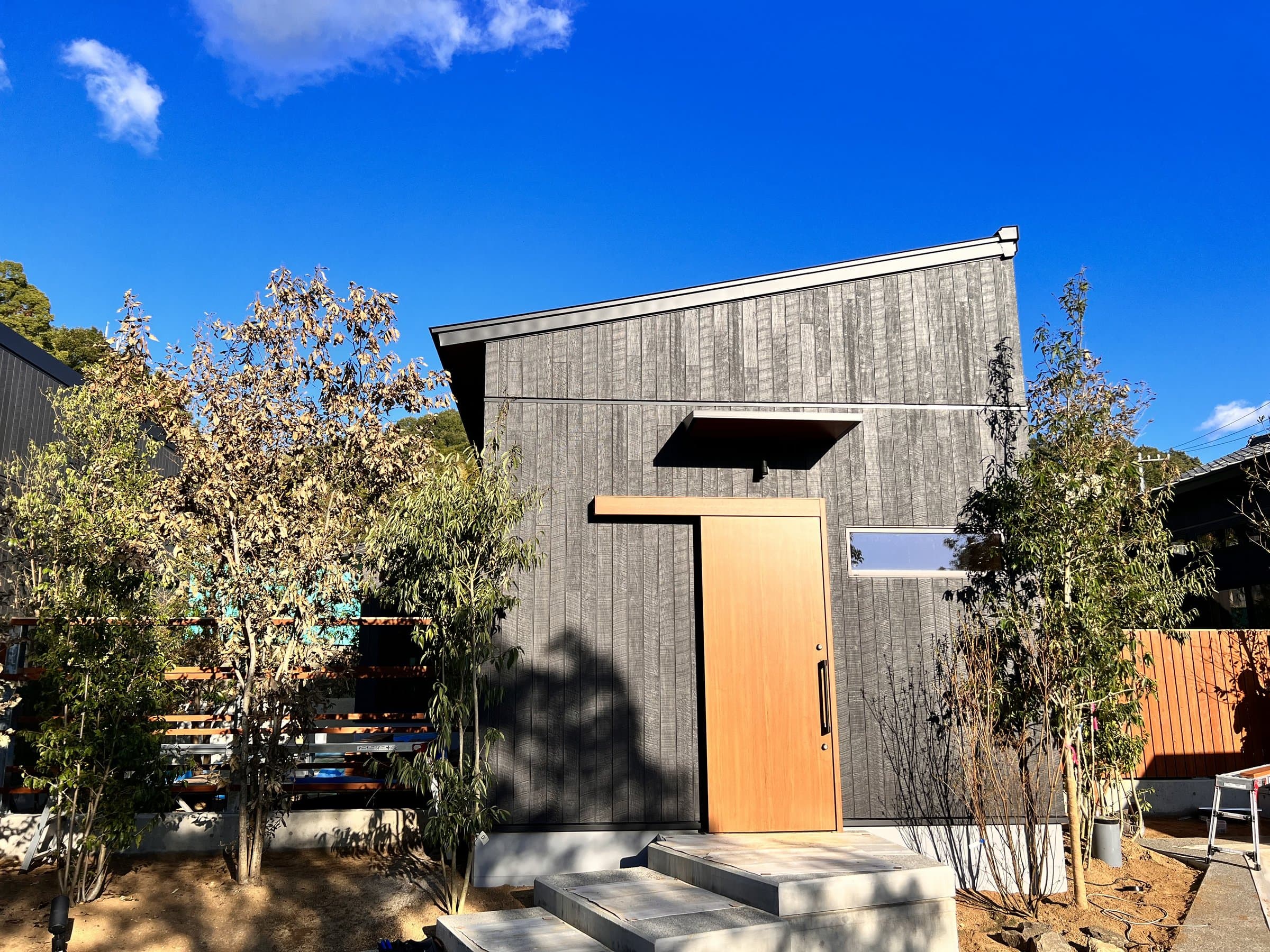 Exterior entrance of Yamanote Bettei Hagakure villa with charred-cedar facade and wooden door under blue sky, Dogo Onsen Matsuyama