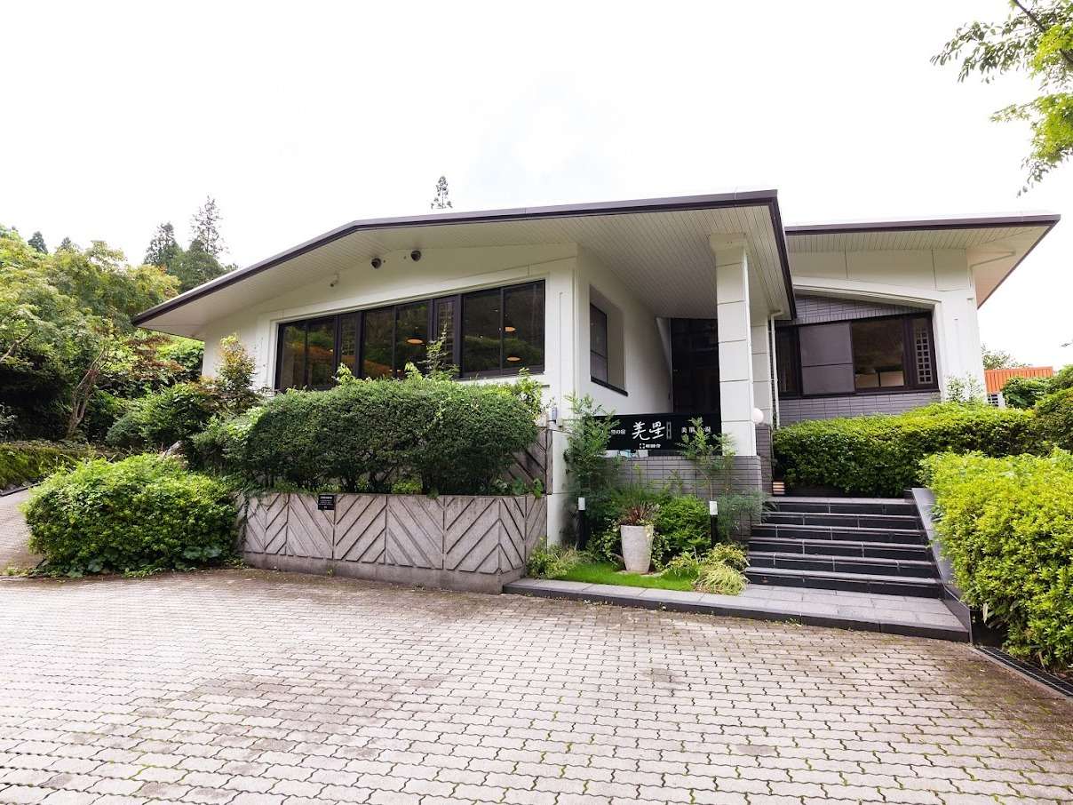 Exterior of Yufudake Ichibo no Yado Bisei ryokan in Yufuin, low white building with paved entrance courtyard and greenery