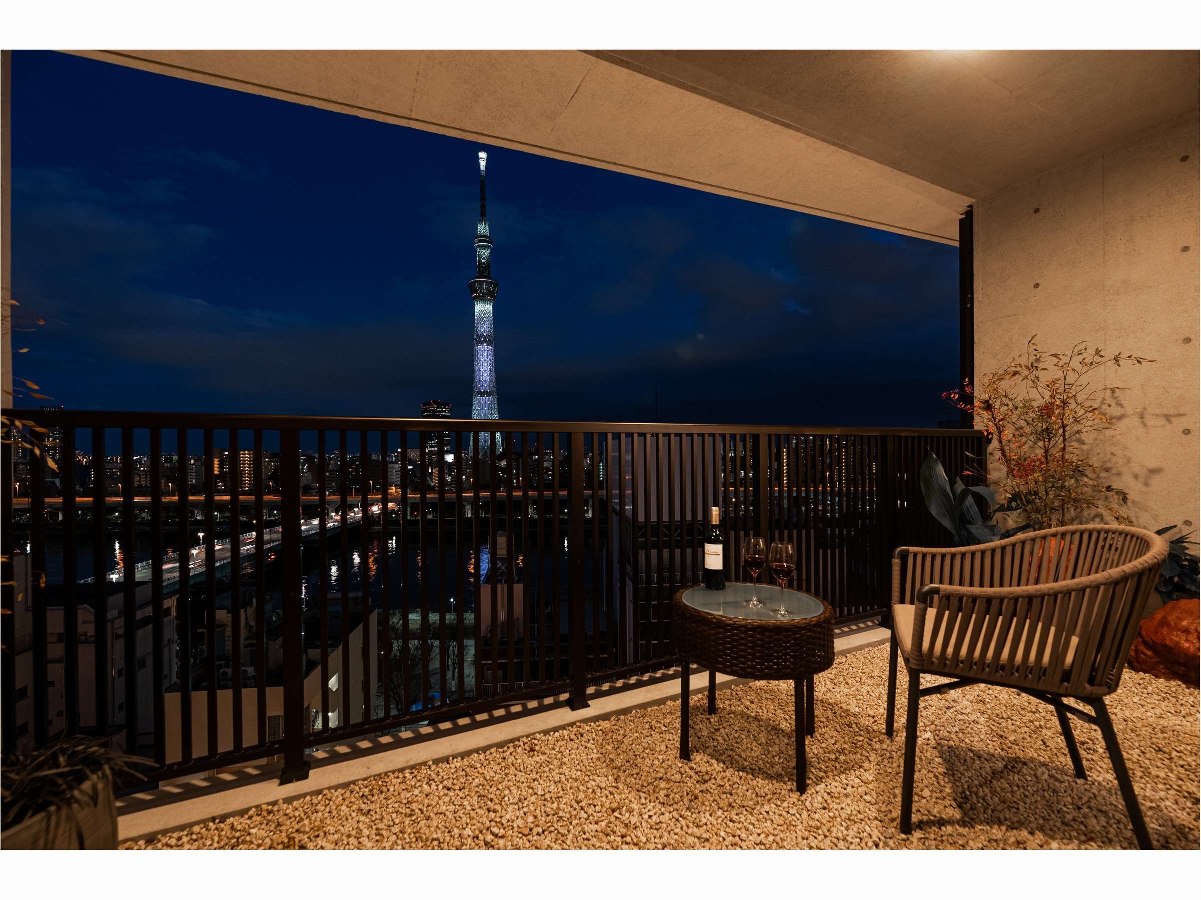 Guest room balcony with armchair overlooking Tokyo Skytree lit up against the night sky in Asakusa