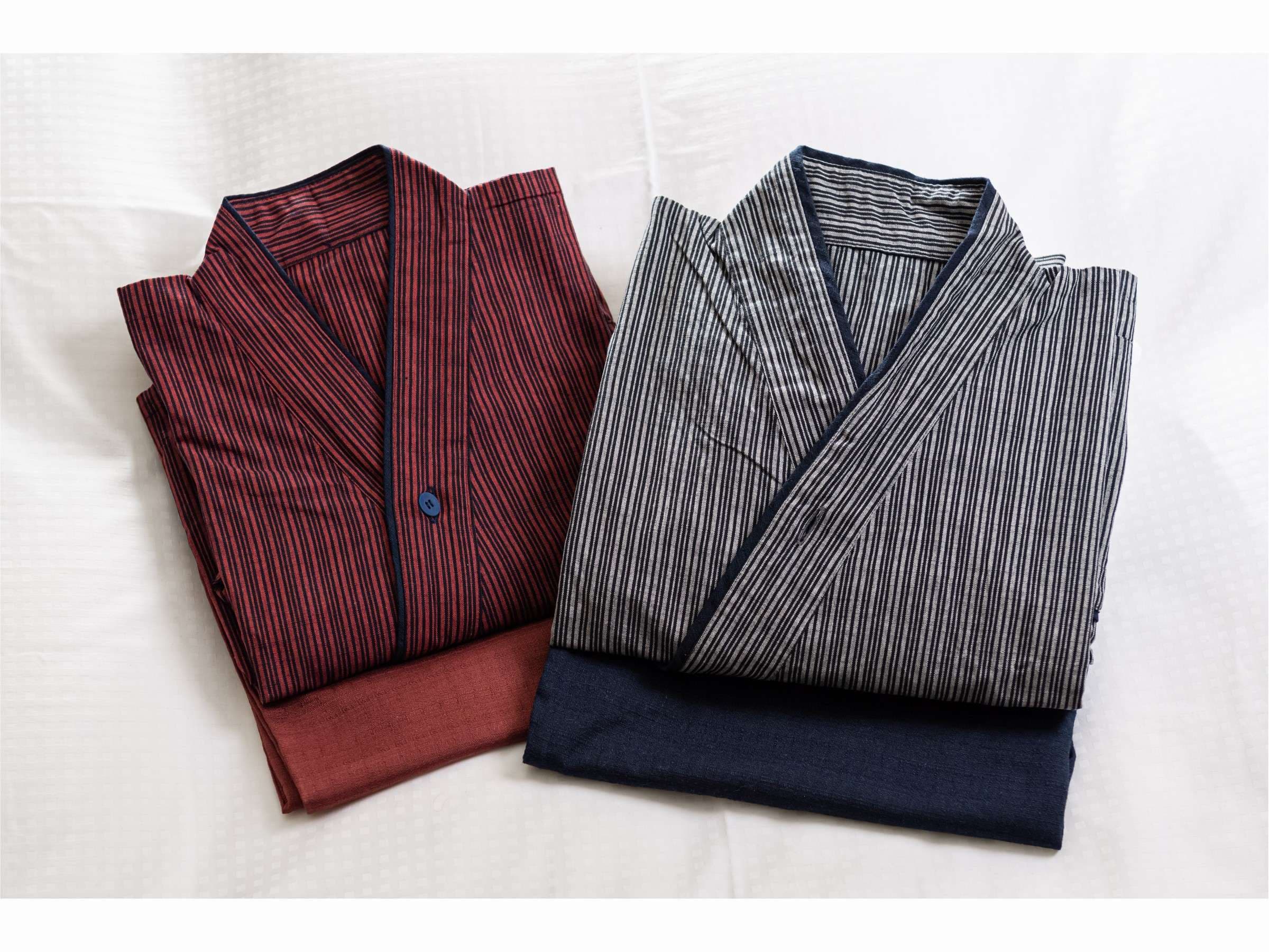 Two folded striped cotton samue robes, one crimson and one indigo, laid on white bedding