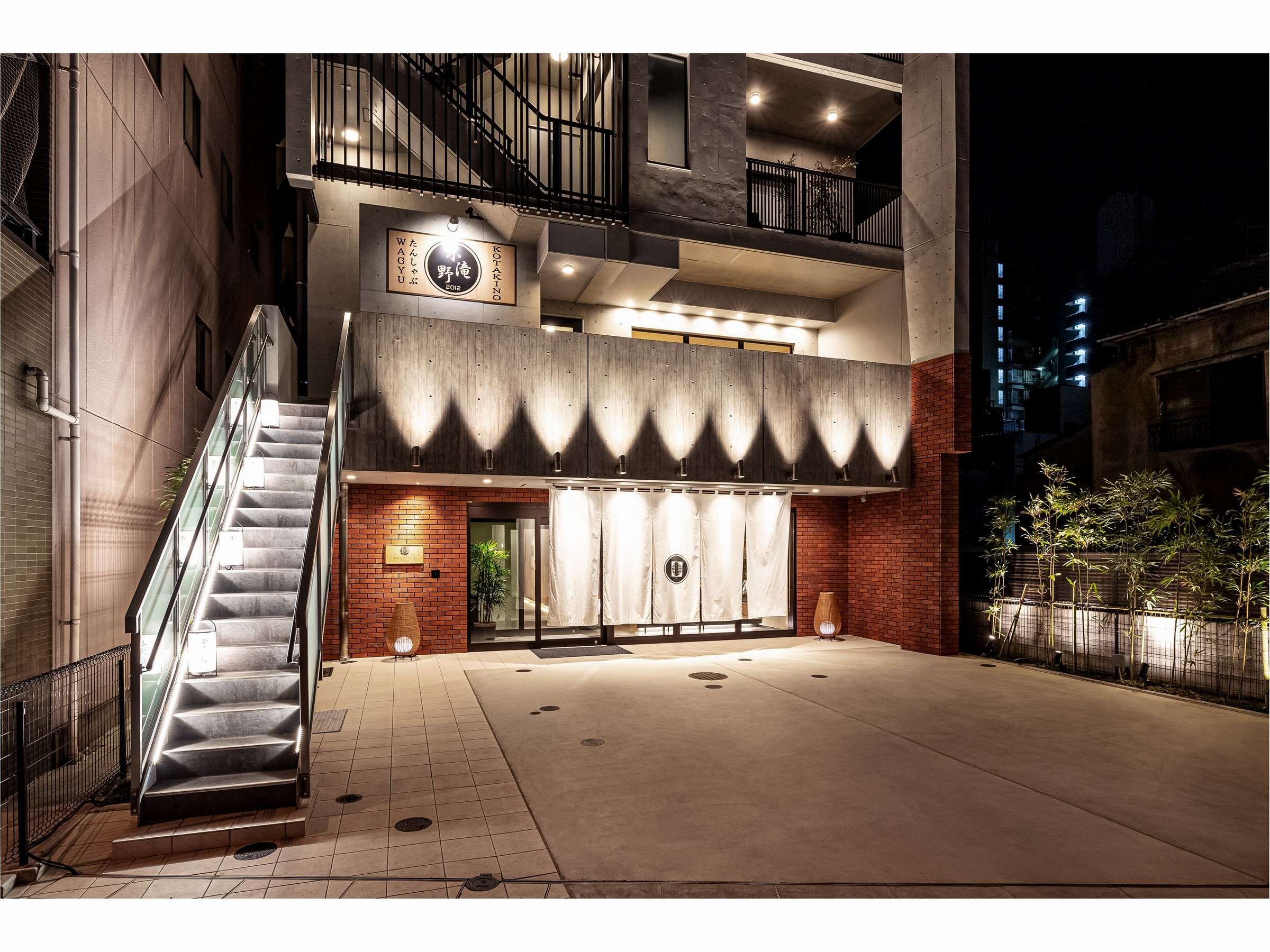 Prostyle Ryokan Tokyo Asakusa illuminated concrete-and-brick entrance with white noren at night