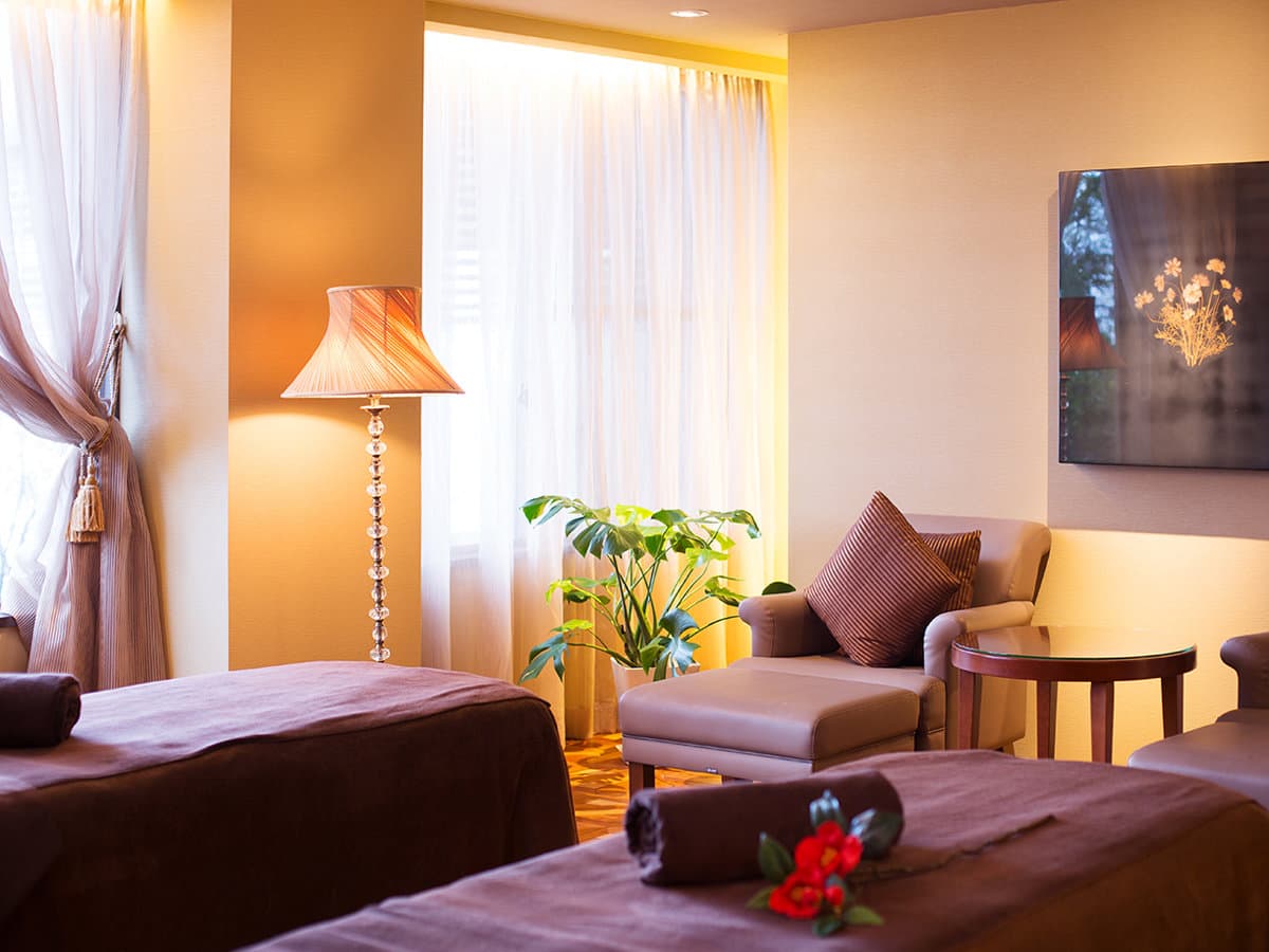 Warmly lit spa treatment room with twin beds and lounge chair at Kissho Caren