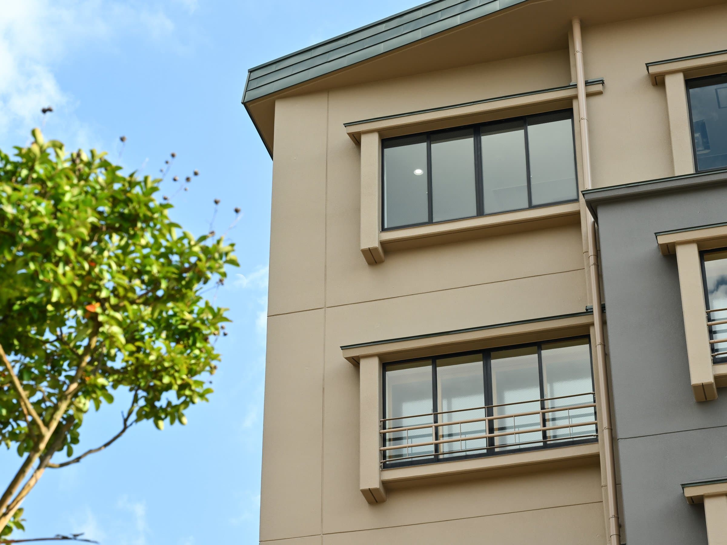 Upper-floor corner of Hamazuru's exterior with guest-room windows against a clear sky at Wakura Onsen