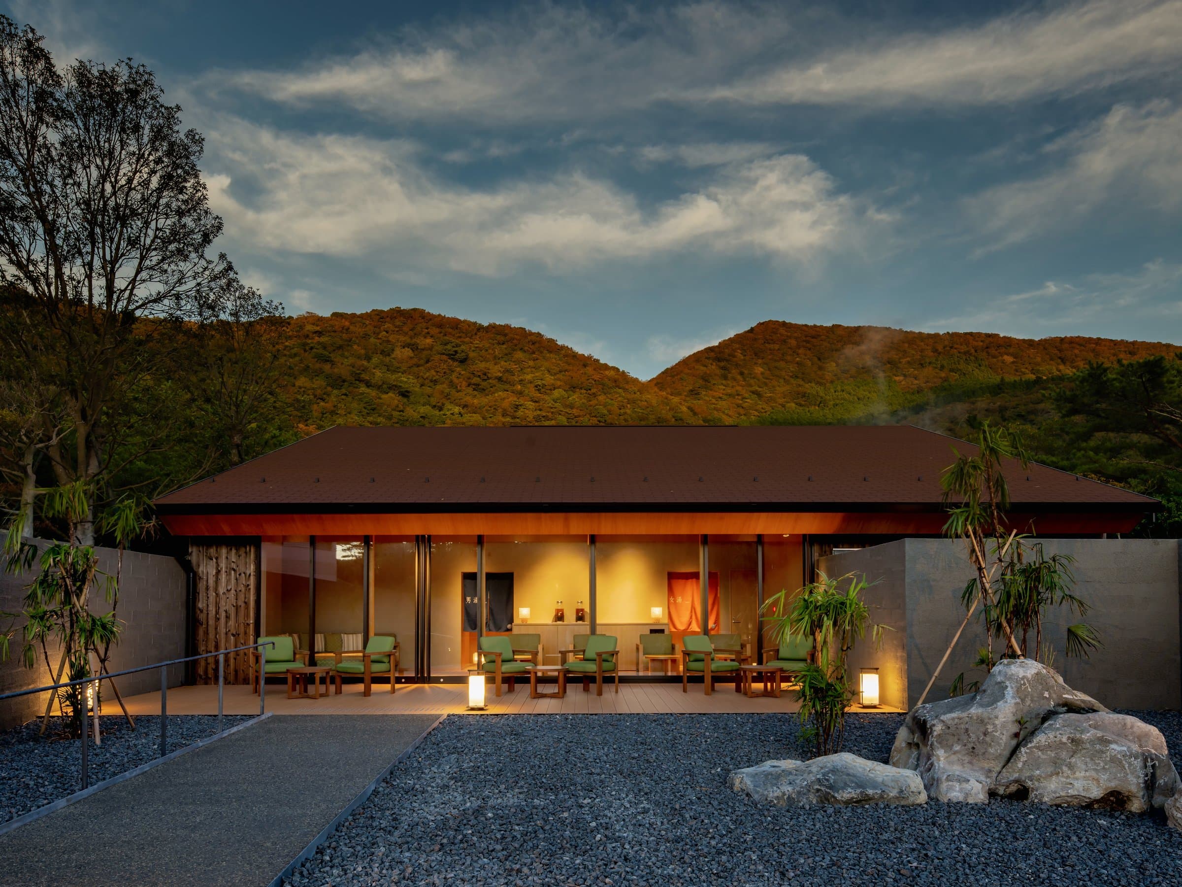 Hoshino Resorts KAI Unzen pavilion exterior at dusk, lit lounge terrace framed by the wooded Unzen Onsen hills in Nagasaki