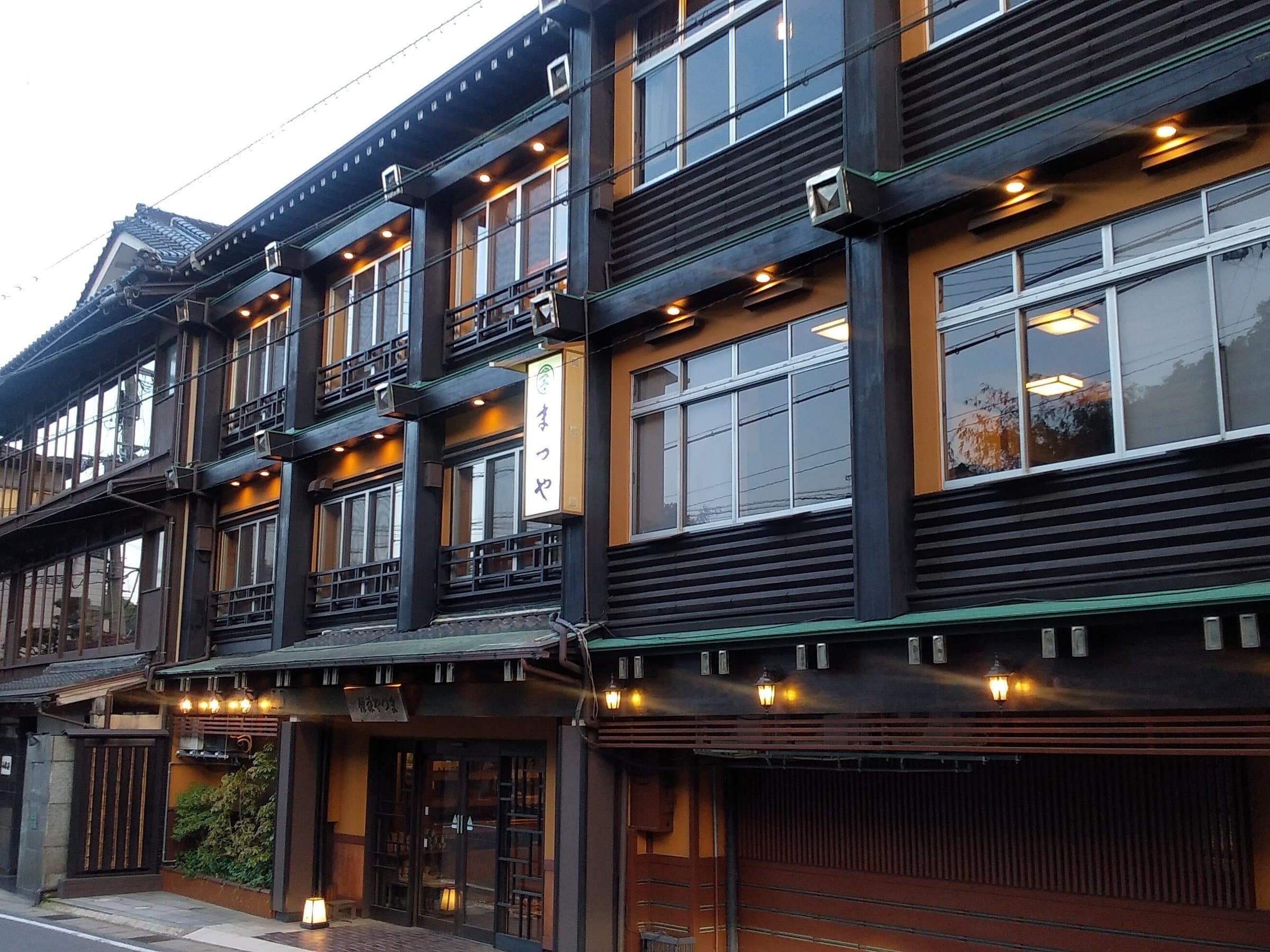 Matsuya ryokan dark timber three-story facade with lit lanterns at dusk in Kinosaki Onsen