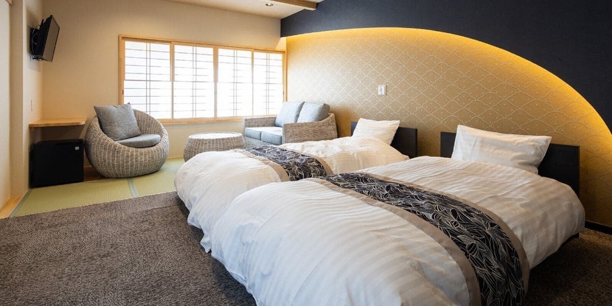 Renovated Japanese-Western guest room at Suehiroya Ryokan with twin beds, a gold scallop-patterned headboard wall and a rattan armchair