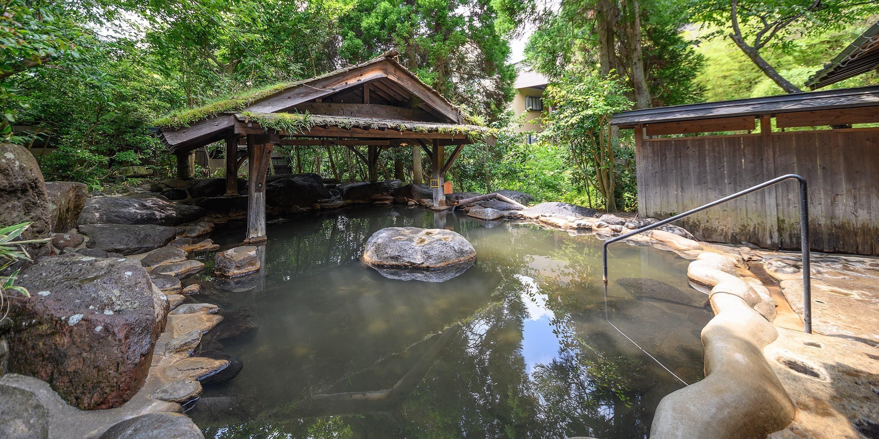 Yumerindo Rindou-no-yu thatched-roof open-air rotenburo set among rocks and lush greenery, Kurokawa Onsen