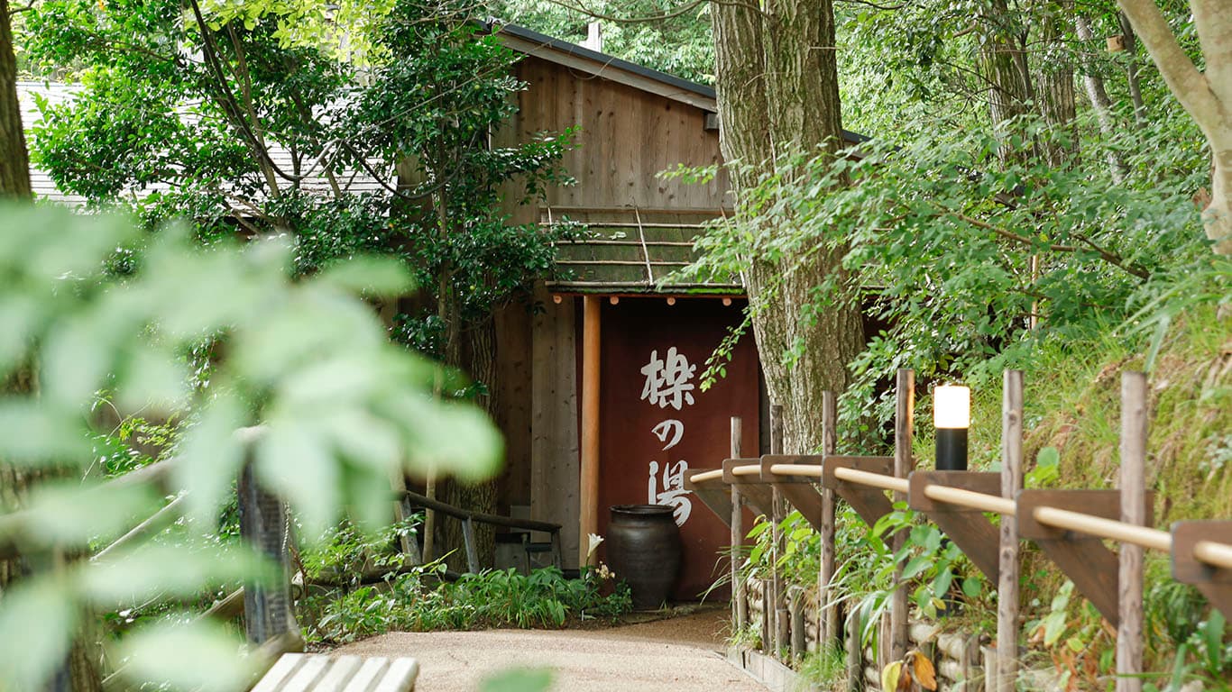 Rustic timber Hotaru-no-Yu bathhouse entrance with hanging noren amid greenery at Ginsuiso Choraku