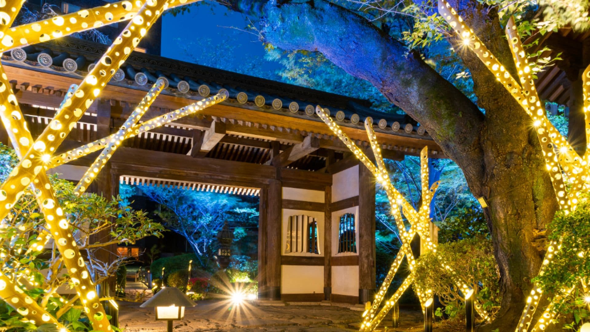 Illuminated traditional wooden gate and garden trees lit up at dusk at Takanawa Hanakohro luxury ryokan annex in Tokyo