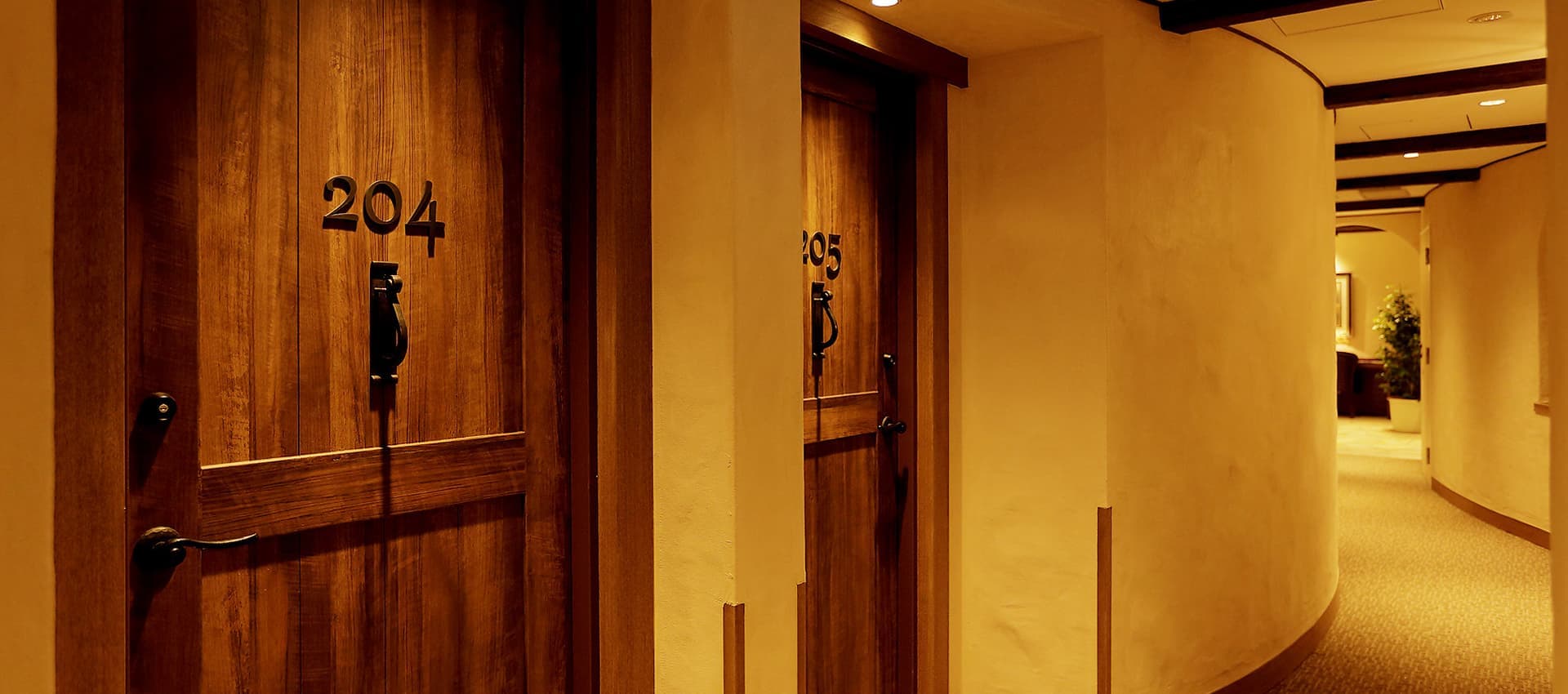 Warmly lit interior corridor at La Vista Fuji Kawaguchiko with wooden guest-room doors and curved plaster walls