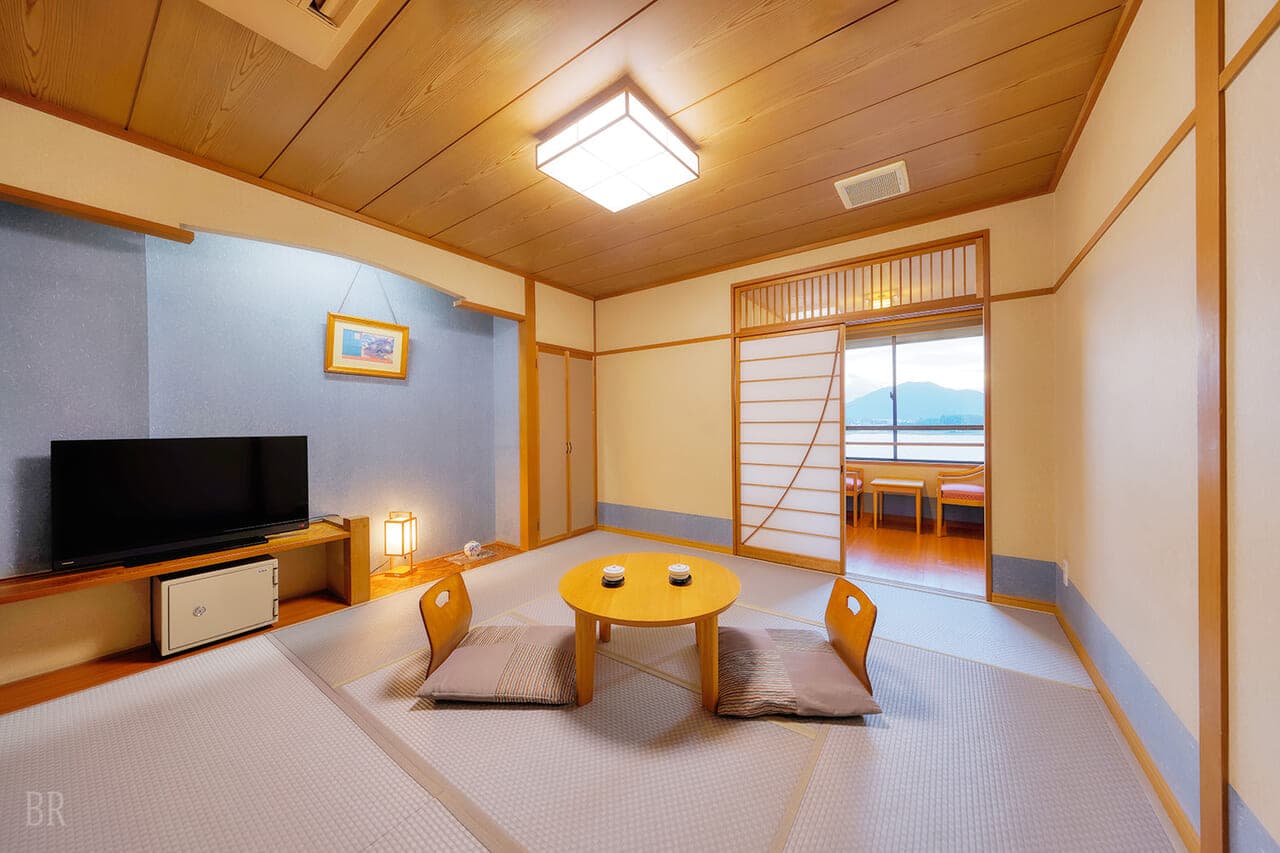 Hotel Asafuji tatami guest room interior looking through floor-to-ceiling window at Mt. Fuji and Lake Kawaguchi in morning light