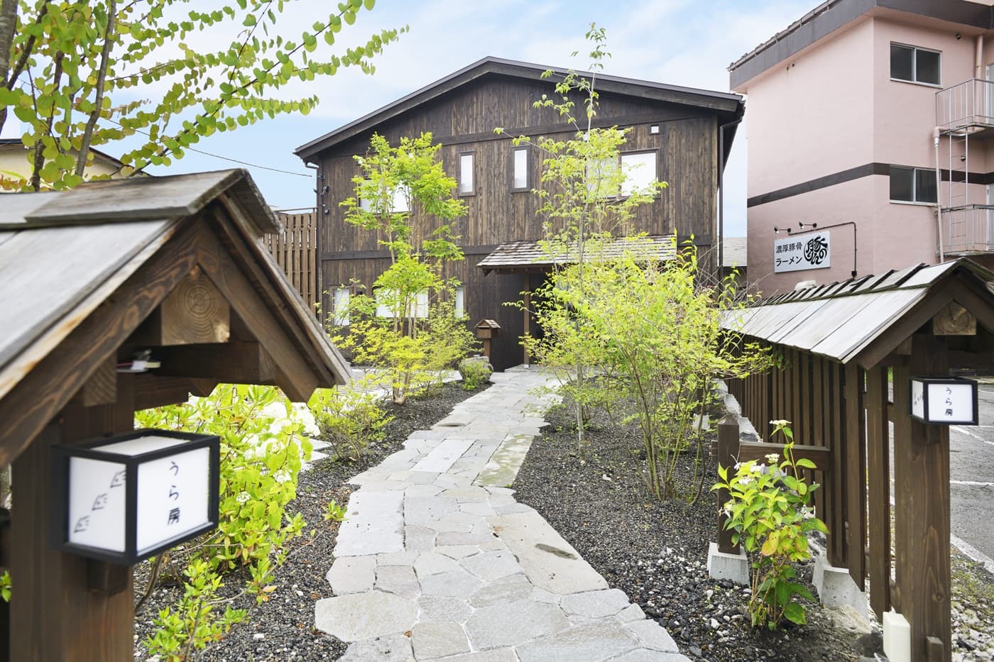 Dark-timber inn exterior with a stone garden path lined by wooden lanterns and fresh greenery