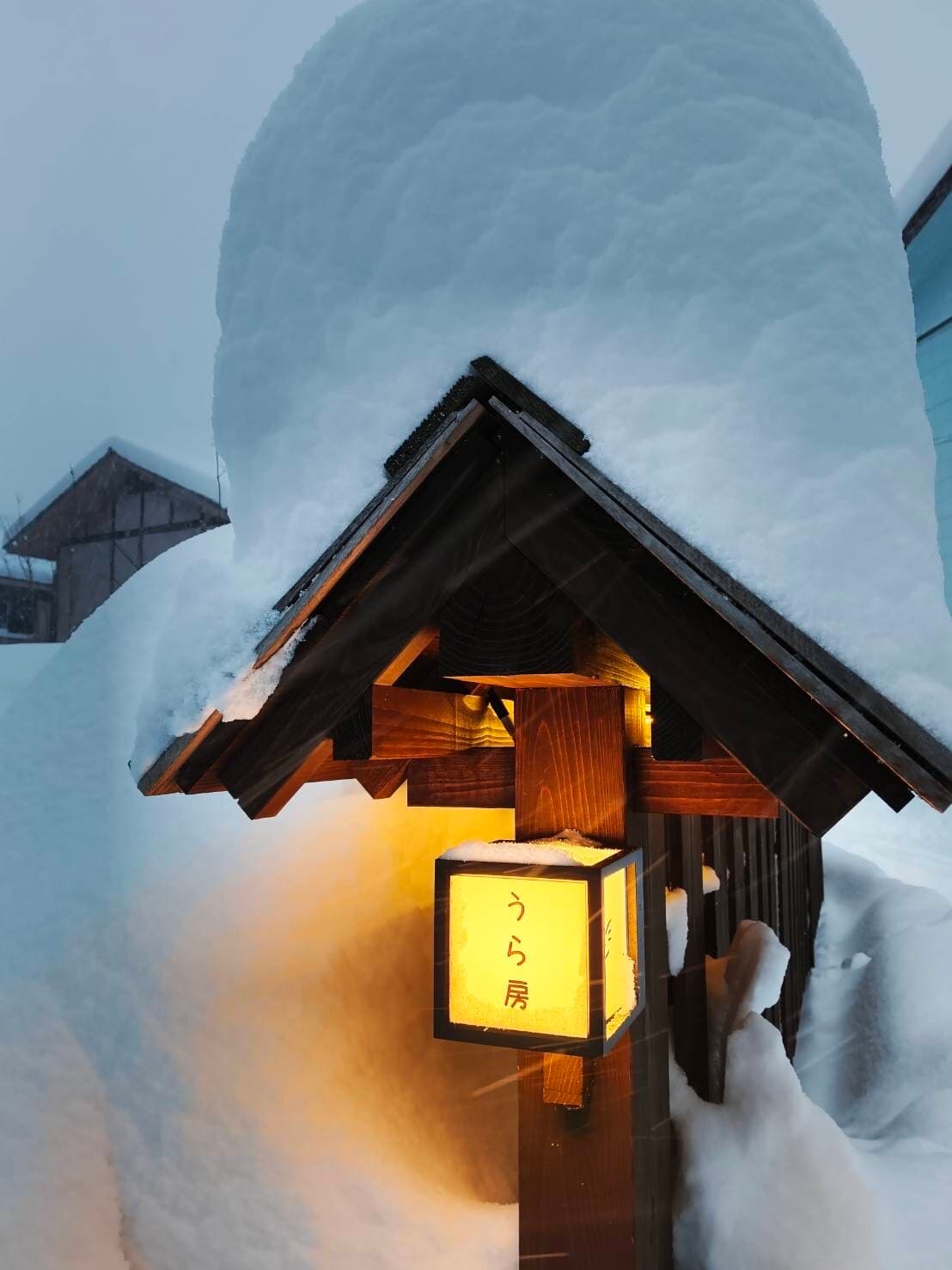 Glowing wooden entrance lantern under deep snow at the inn's gabled gate in winter