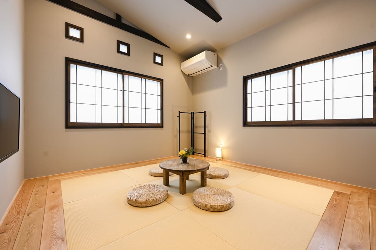 Bright tatami guest room with low round table, woven cushions and twin shoji-style windows