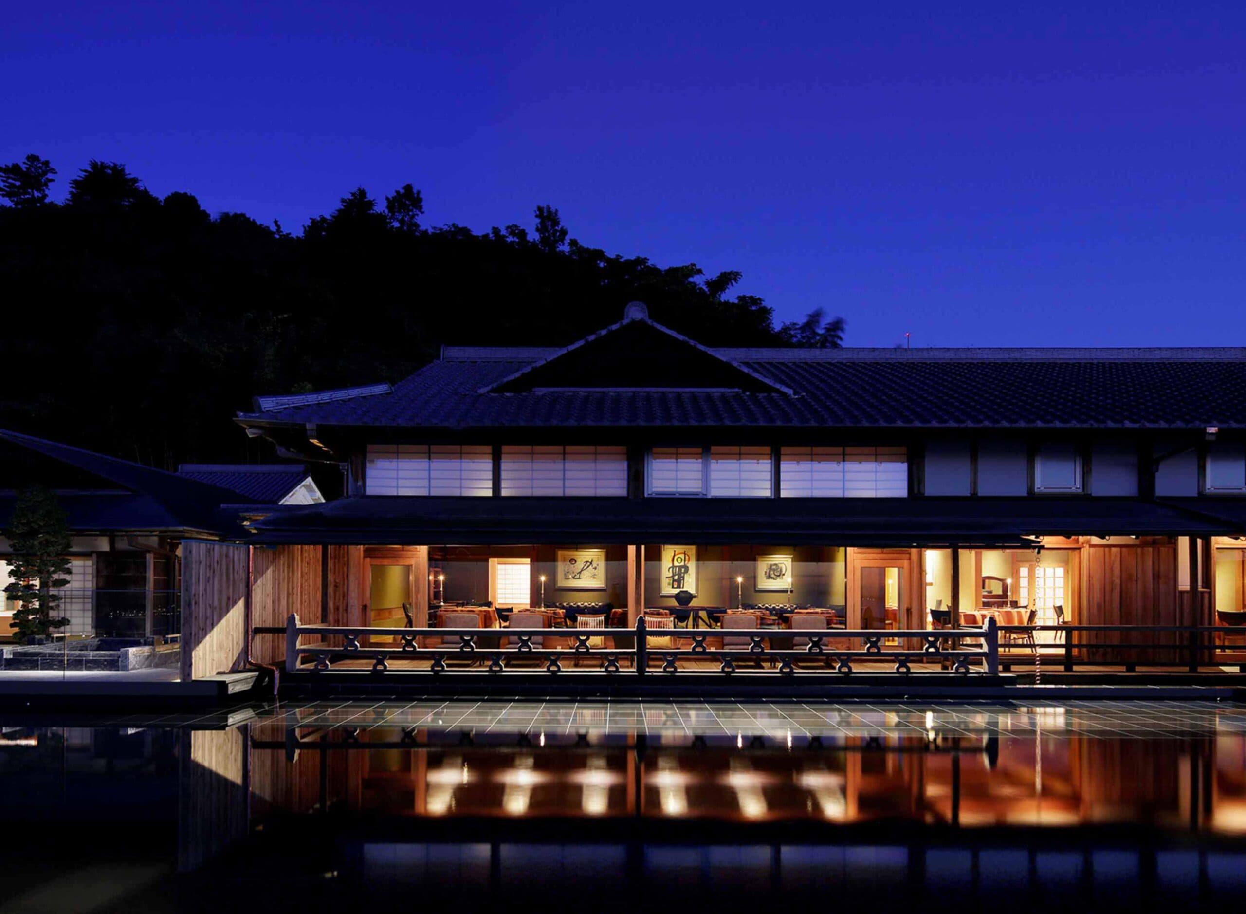 The Hiramatsu Hotels & Resorts Atami traditional wooden main building lit at dusk, mirrored in a reflecting pool above Sagami Bay