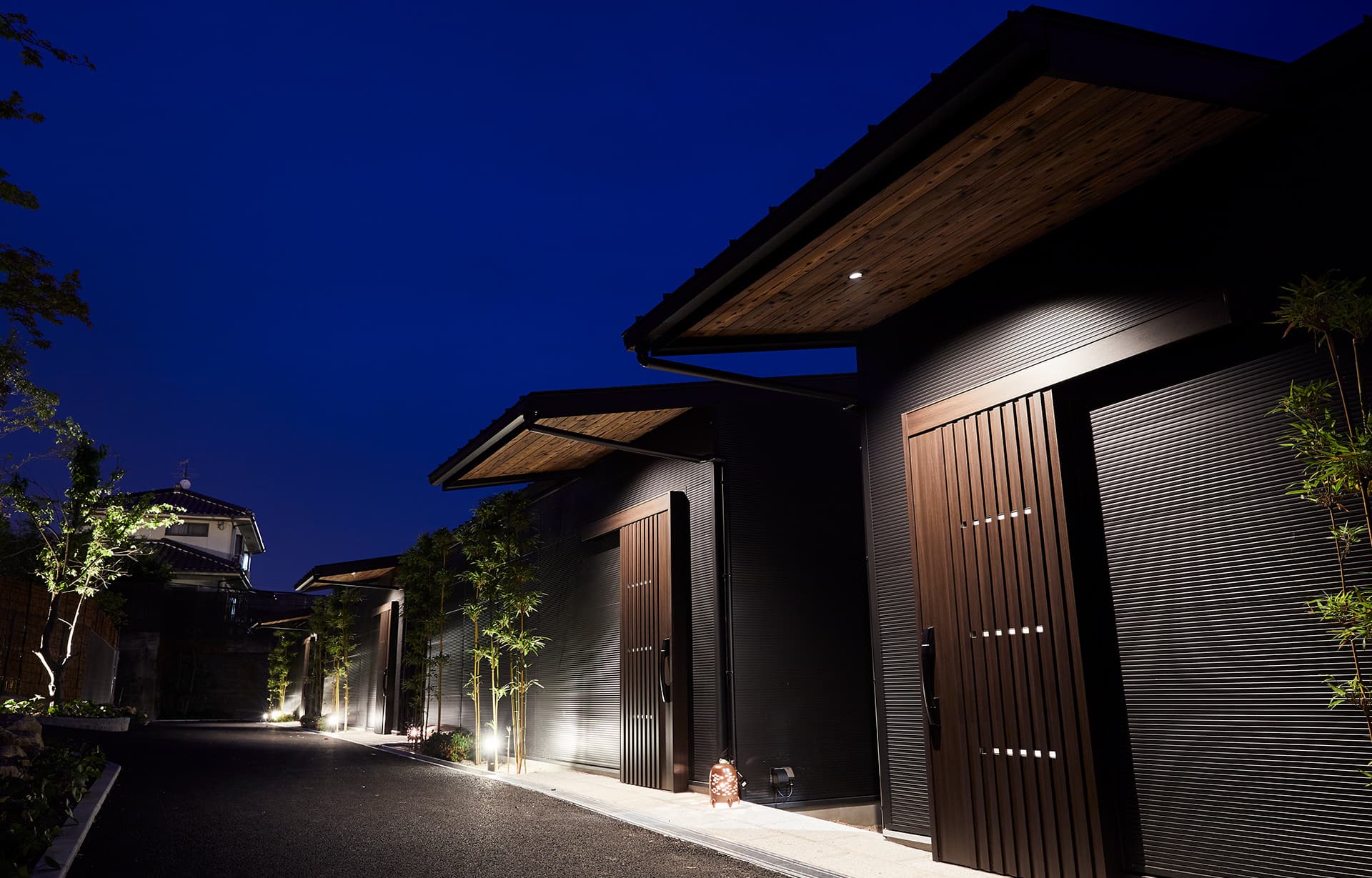 Row of private detached villas at IBUKU, a Miyahama Onsen ryokan near Miyajima, lit at dusk with lanterns lining the entrance path
