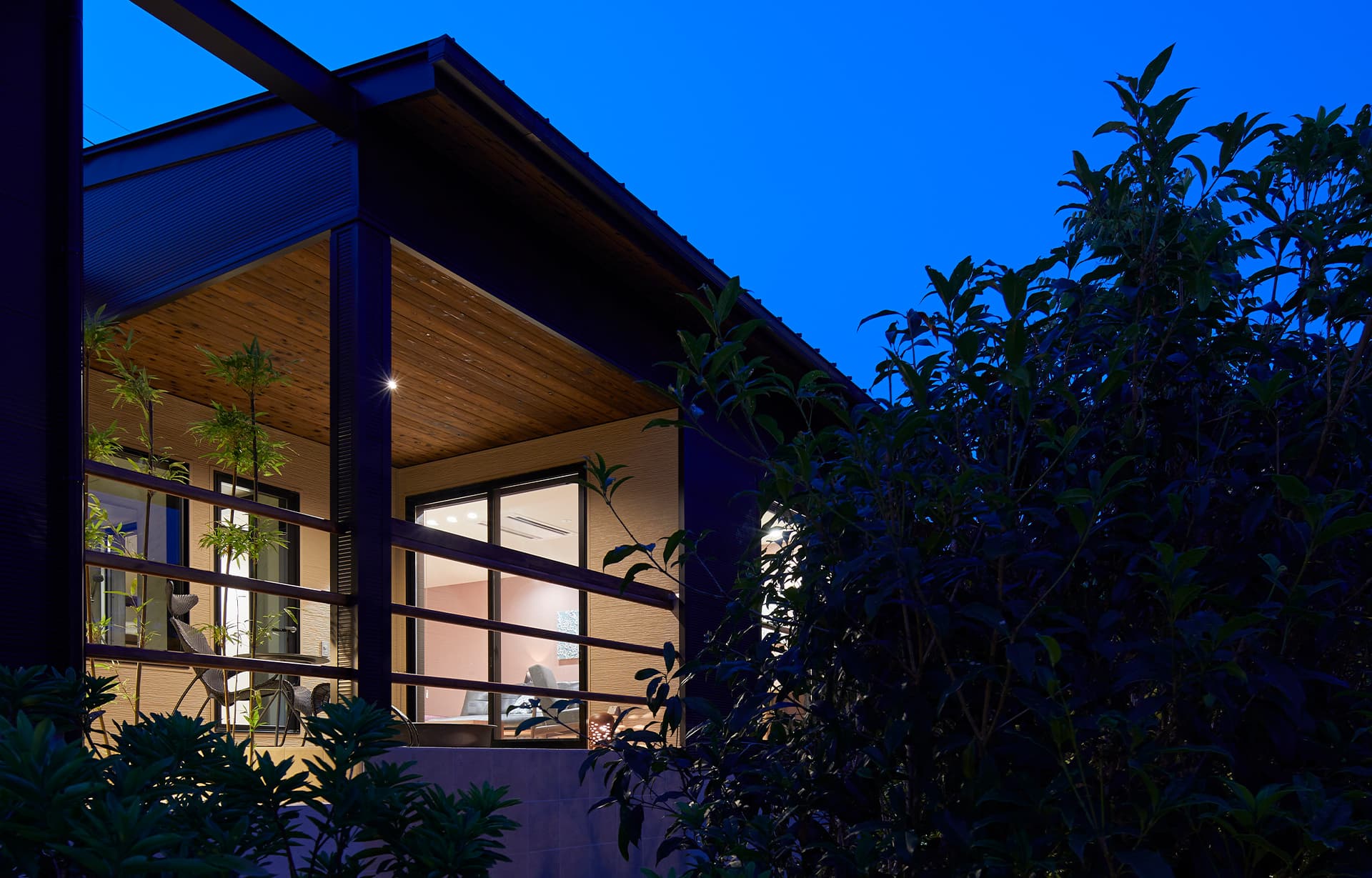 Illuminated detached villa with a wooden-ceiling terrace at IBUKU near Miyajima glowing against a deep blue twilight sky