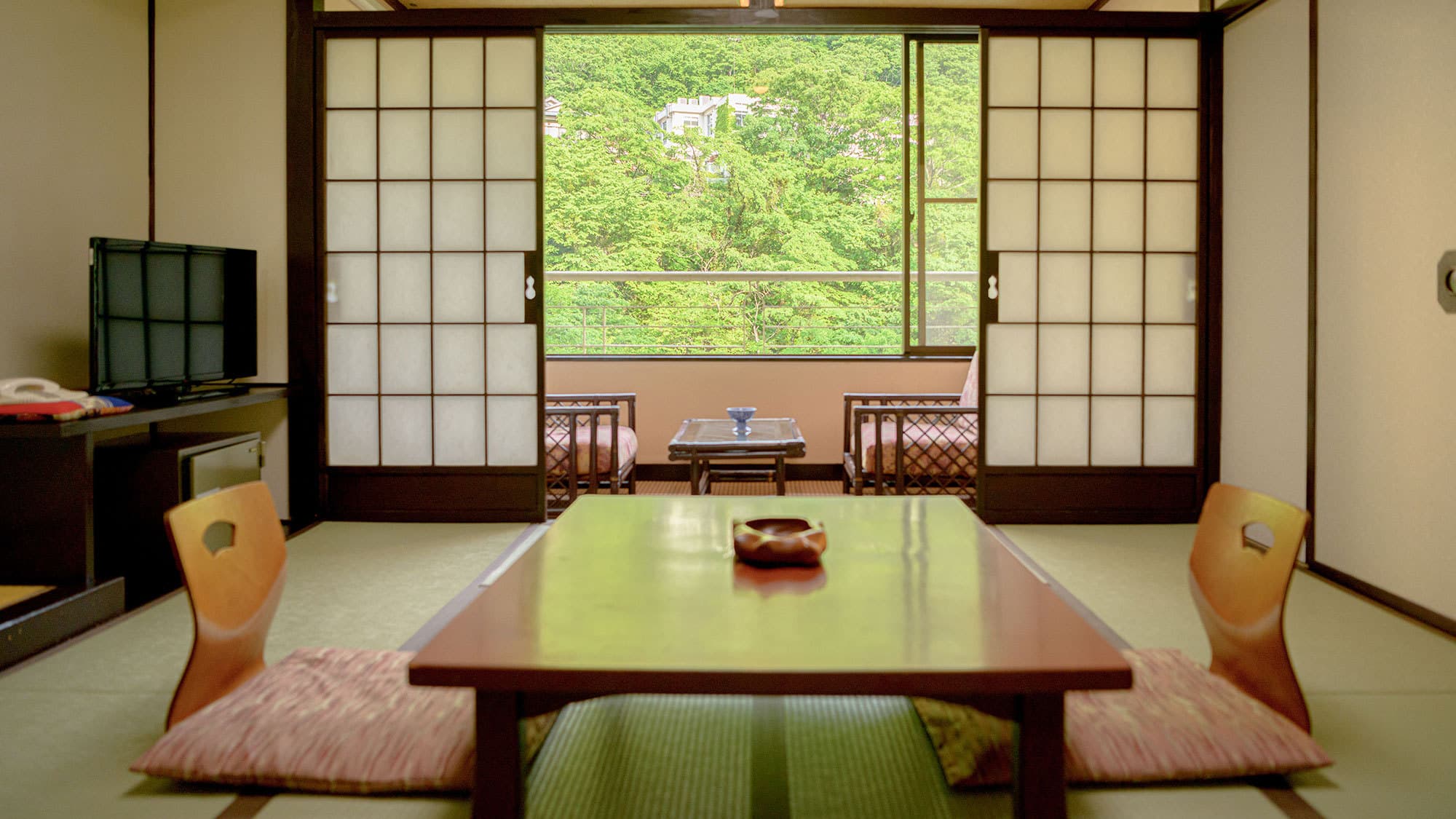 Tatami guest room at Isshinkan with low table, floor chairs and a balcony framing the green Kinugawa valley