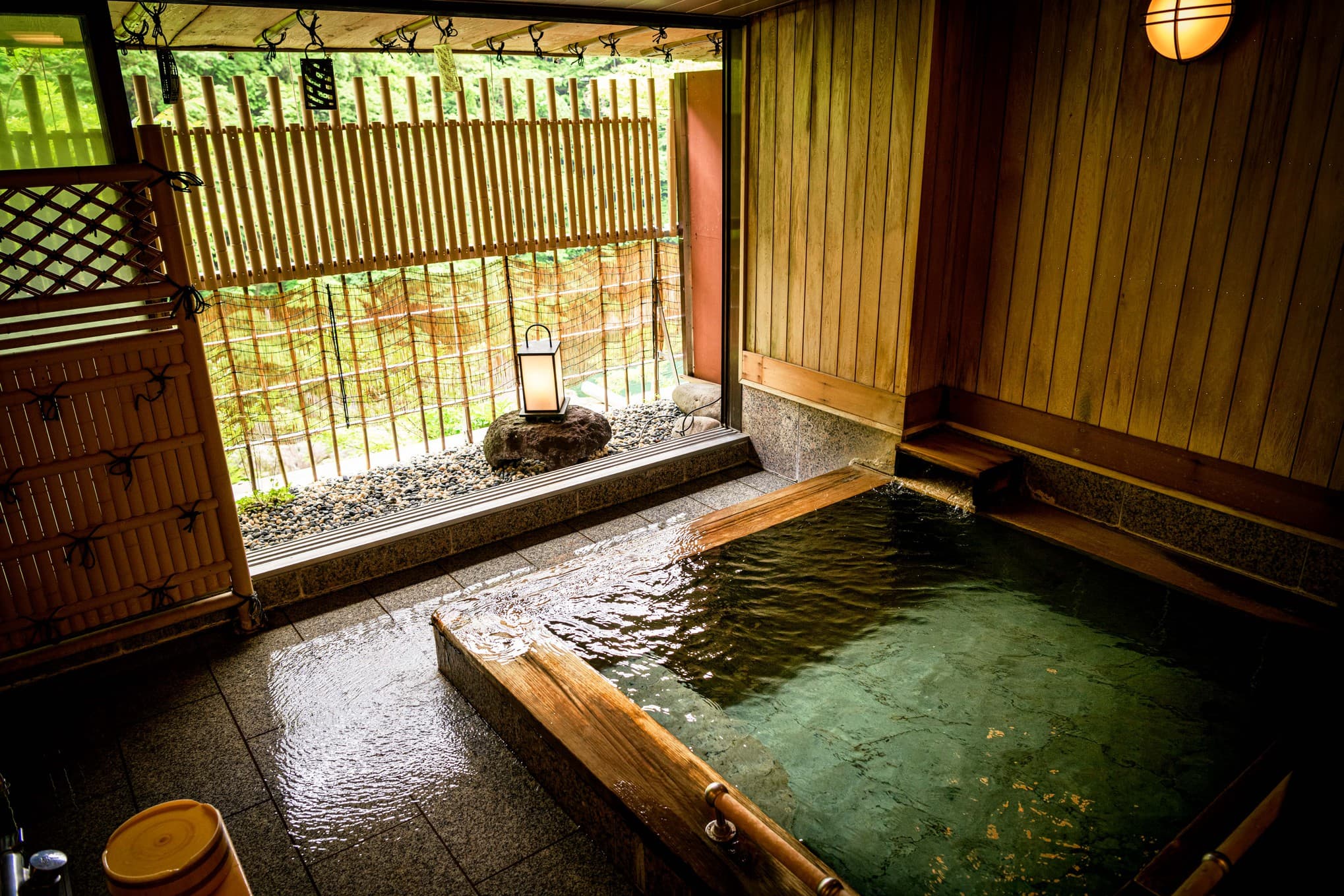 Open-air rotenburo cypress-and-stone hot spring bath at Isshinkan, Kinugawa Onsen, with bamboo fence and lantern view