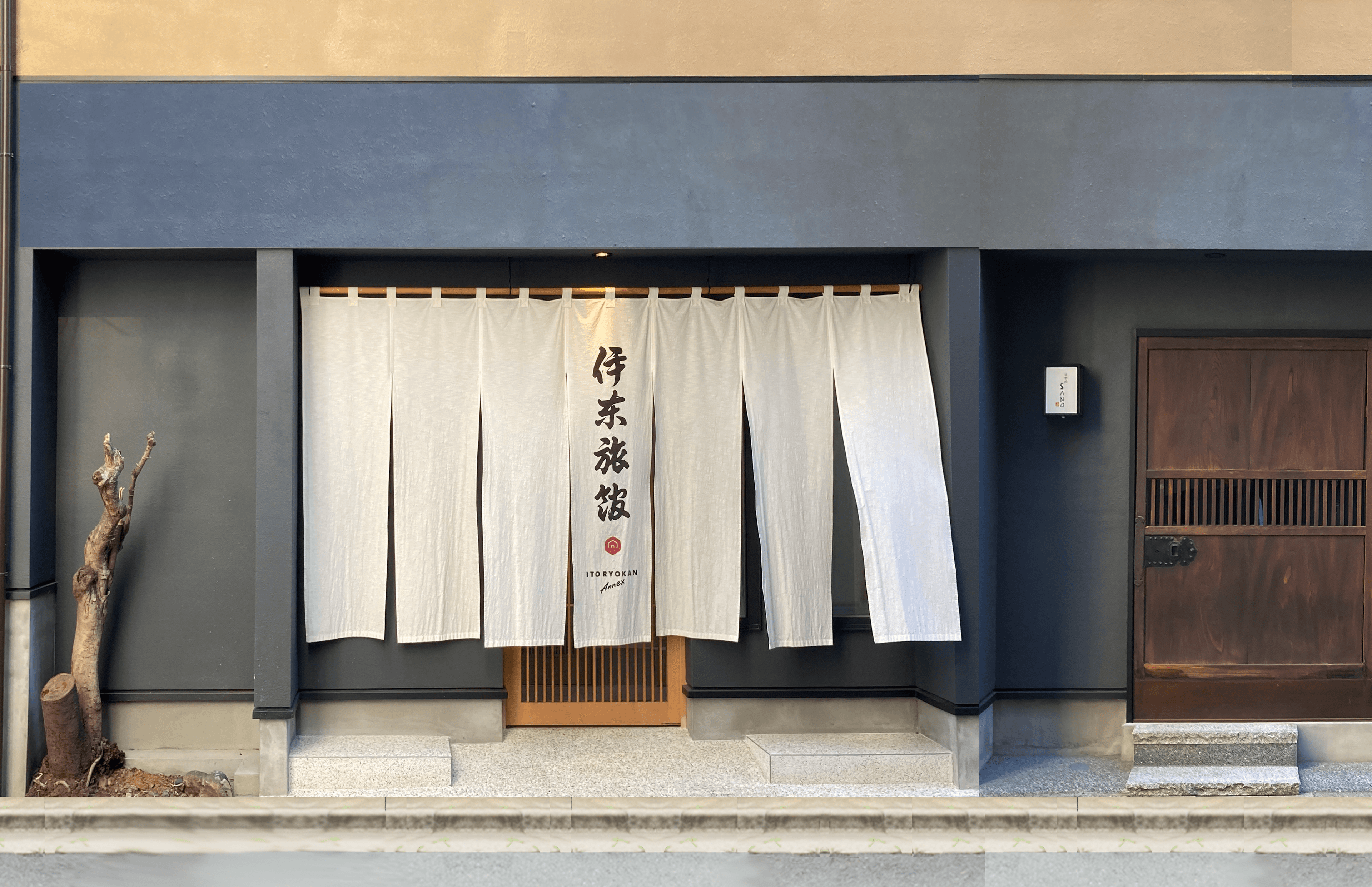 Annex entrance of Ito Ryokan in Nihonbashi Tokyo with white noren curtain under a dark facade