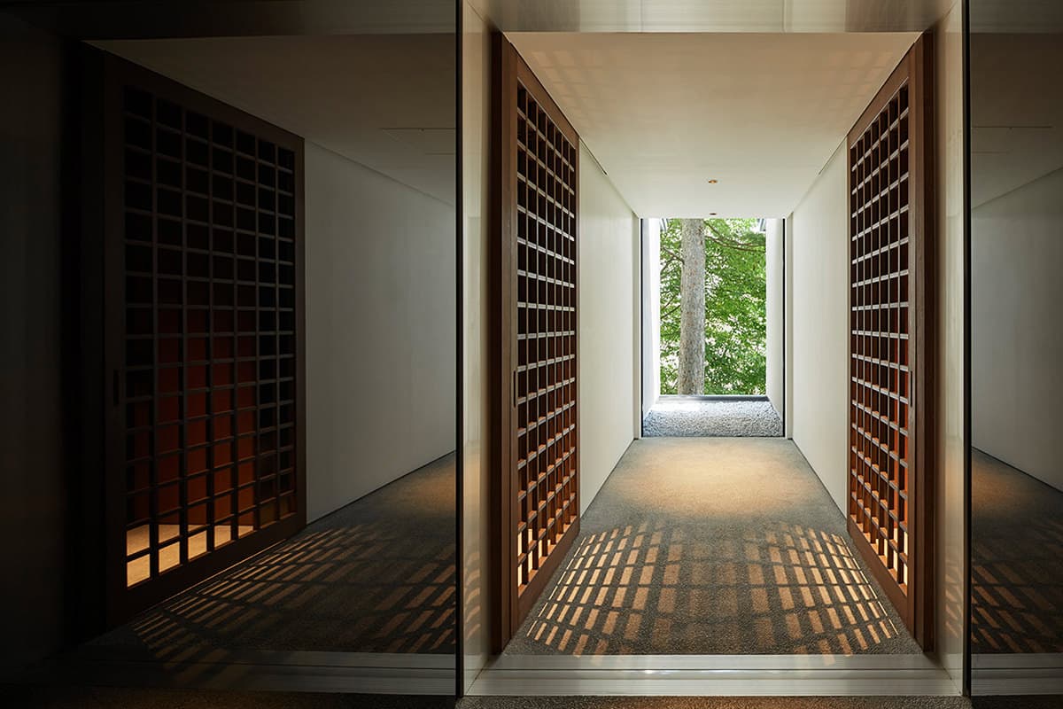 Symmetrical interior corridor with wooden lattice doors opening to a forest view