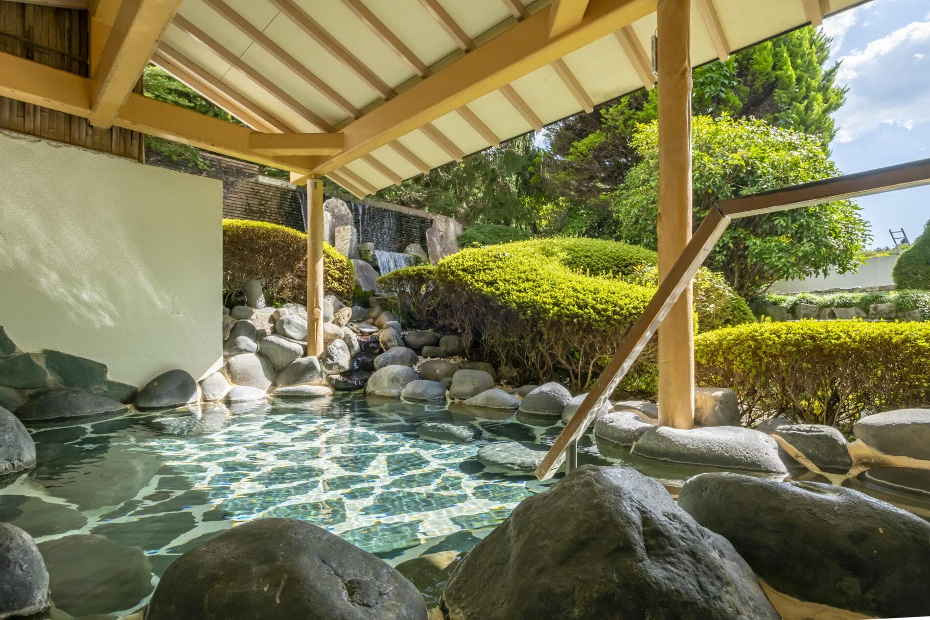 Large open-air rock hot-spring bath with a waterfall and manicured garden