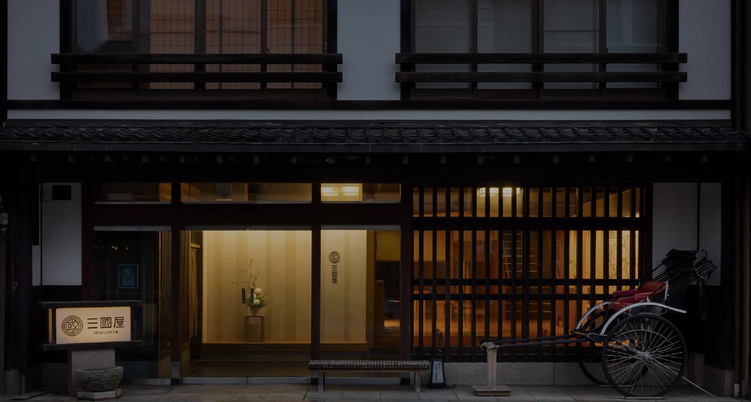 Mikuniya ryokan machiya-style exterior at dusk with rickshaw and illuminated entrance in Kinosaki Onsen