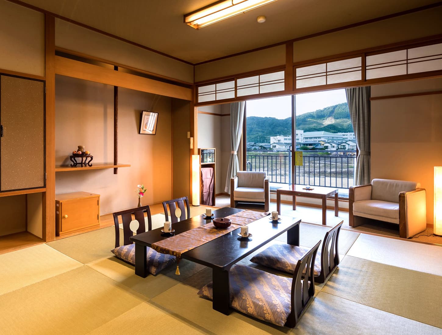 Spacious tatami guest room at Kiyonoya with low dining table, lounge chairs and a river-and-mountain view through wide windows