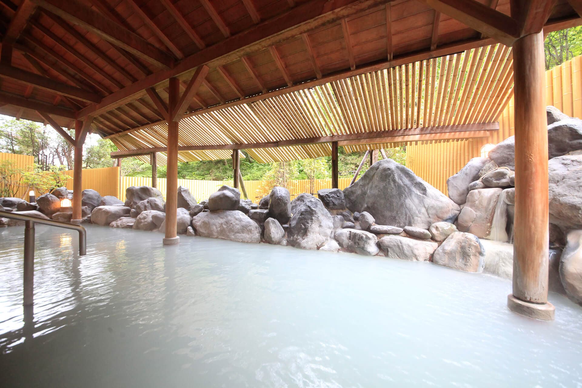 Open-air rotenburo bath with milky sulphur water ringed by natural rocks under a timber roof at Park Hotel Miyabitei in Noboribetsu Onsen