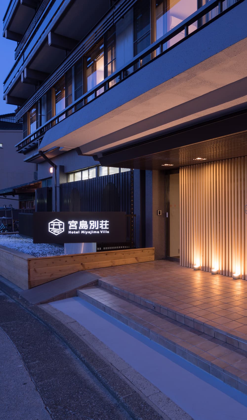 Hotel Miyajima Villa illuminated entrance and facade at dusk with wood-slat doorway on Miyajima island