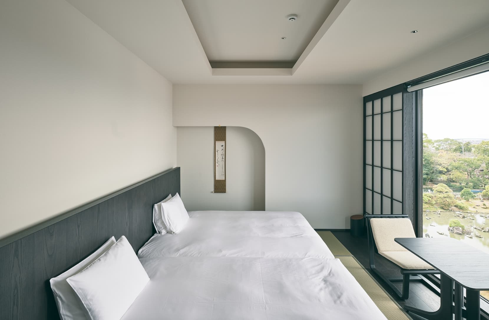 Ohana guest room with twin beds, a hanging calligraphy scroll and a large window overlooking the Shoto-en pond garden in Yanagawa