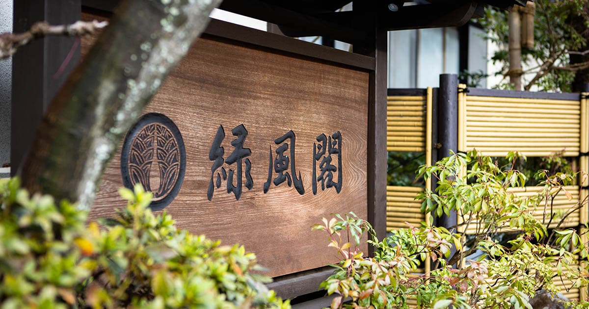 Ryokufukaku ryokan carved wooden entrance name plaque framed by garden greenery