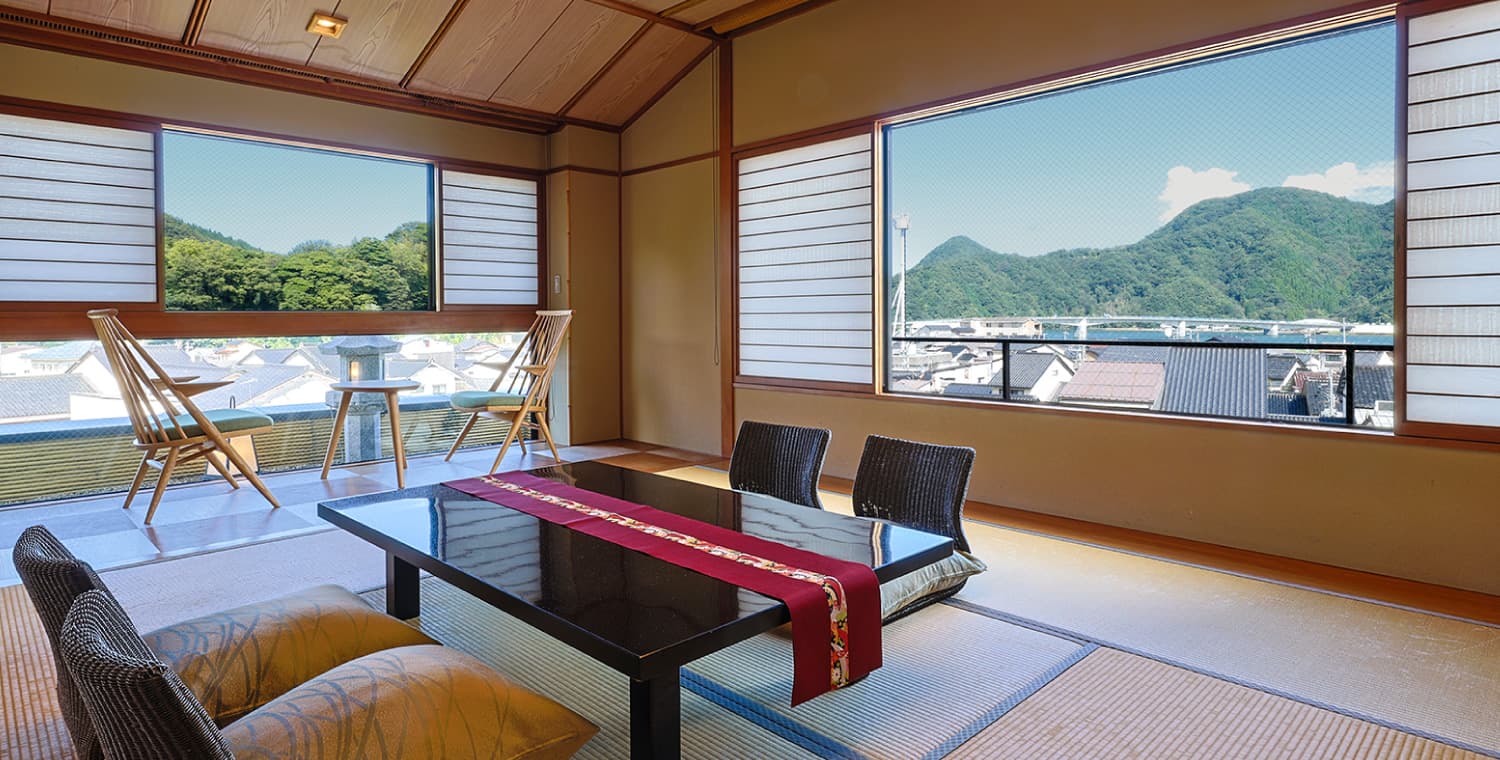 Tatami guest room at Ryokufukaku with low table, red runner and panoramic mountain-and-town view in Kinosaki Onsen