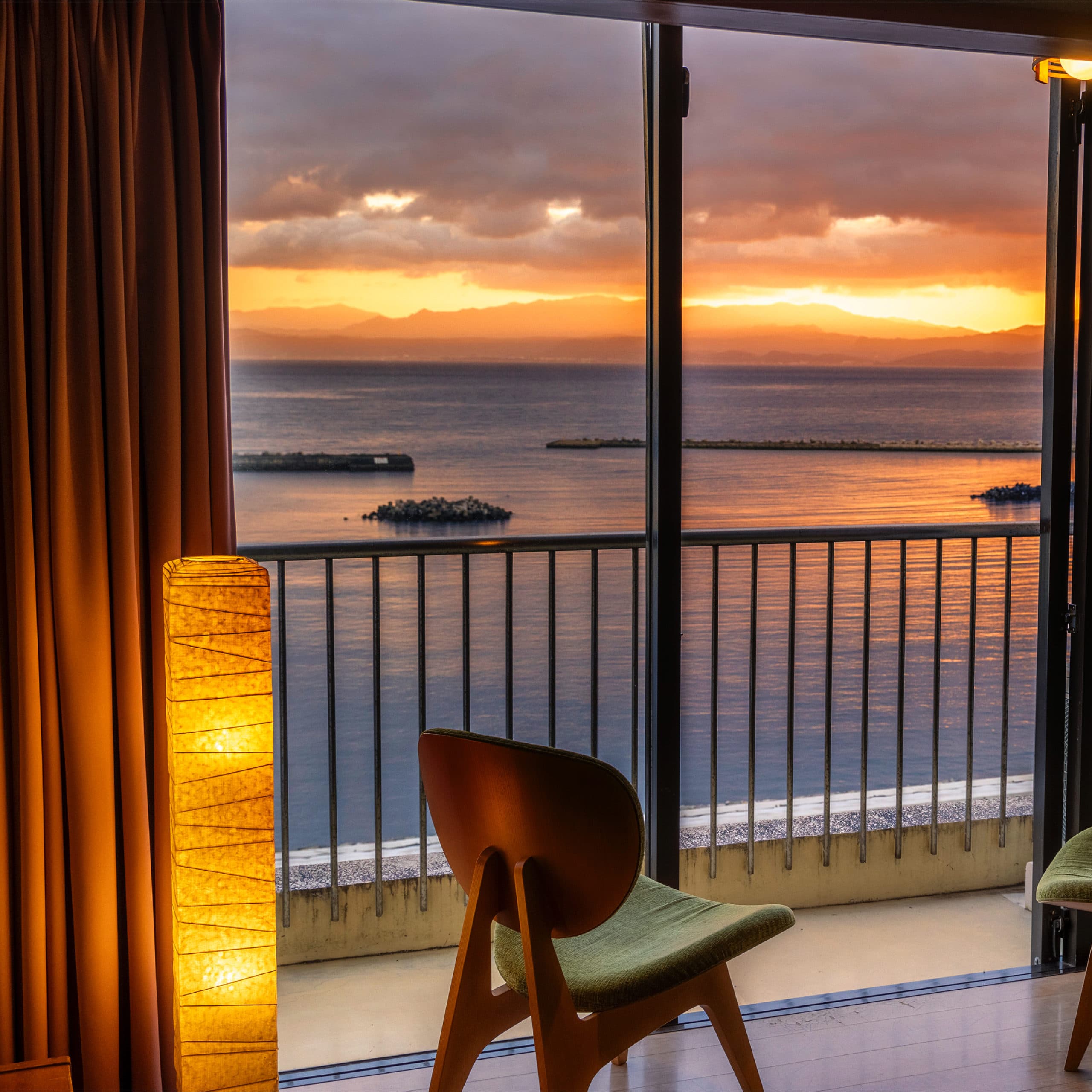 Guest room window seat with paper lamp framing a golden sunset over the bay, Hotel Shougetsu Ibusuki