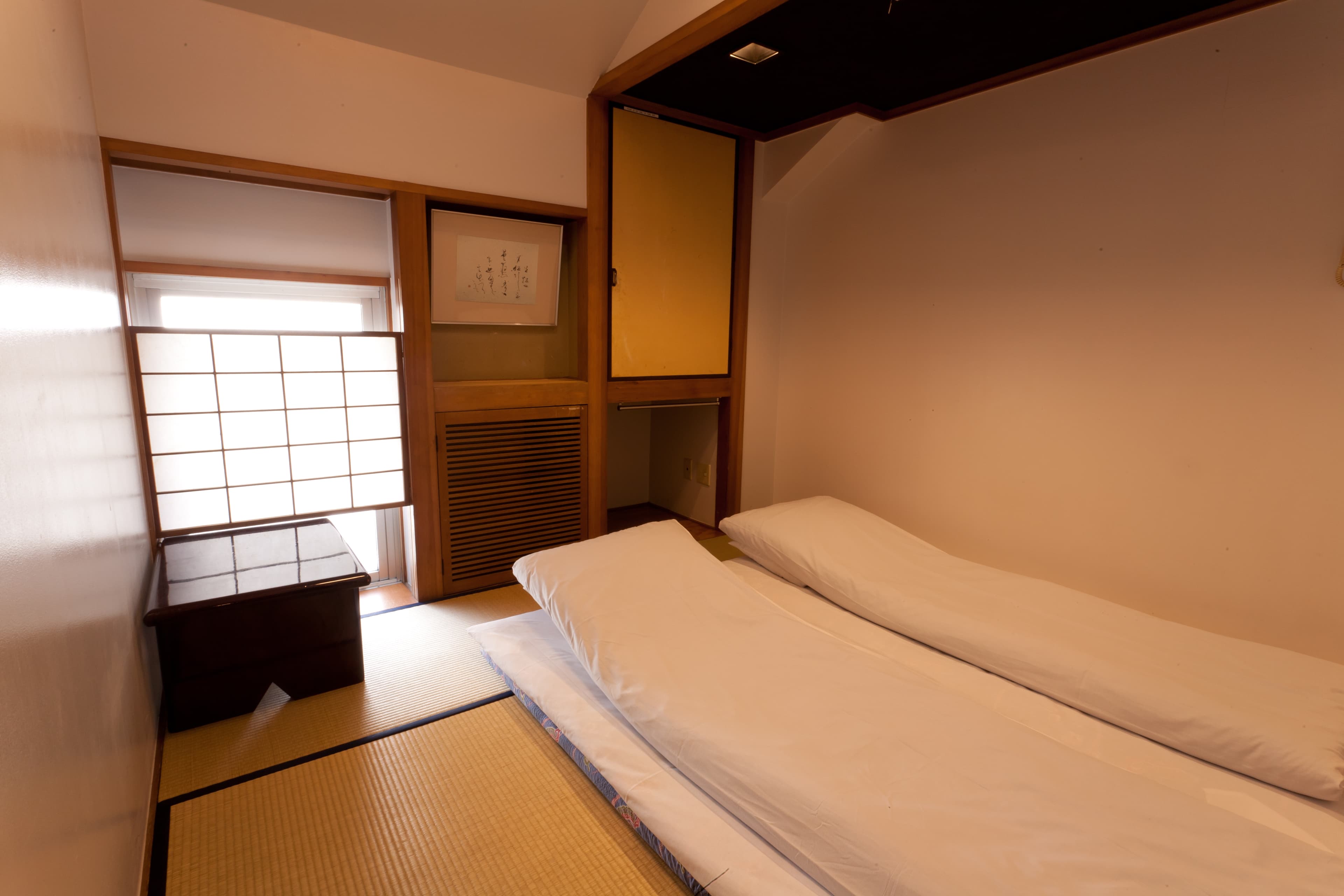 Tatami guest room at Kimi Ryokan with two futons laid out, hanging scroll and shoji-screened window