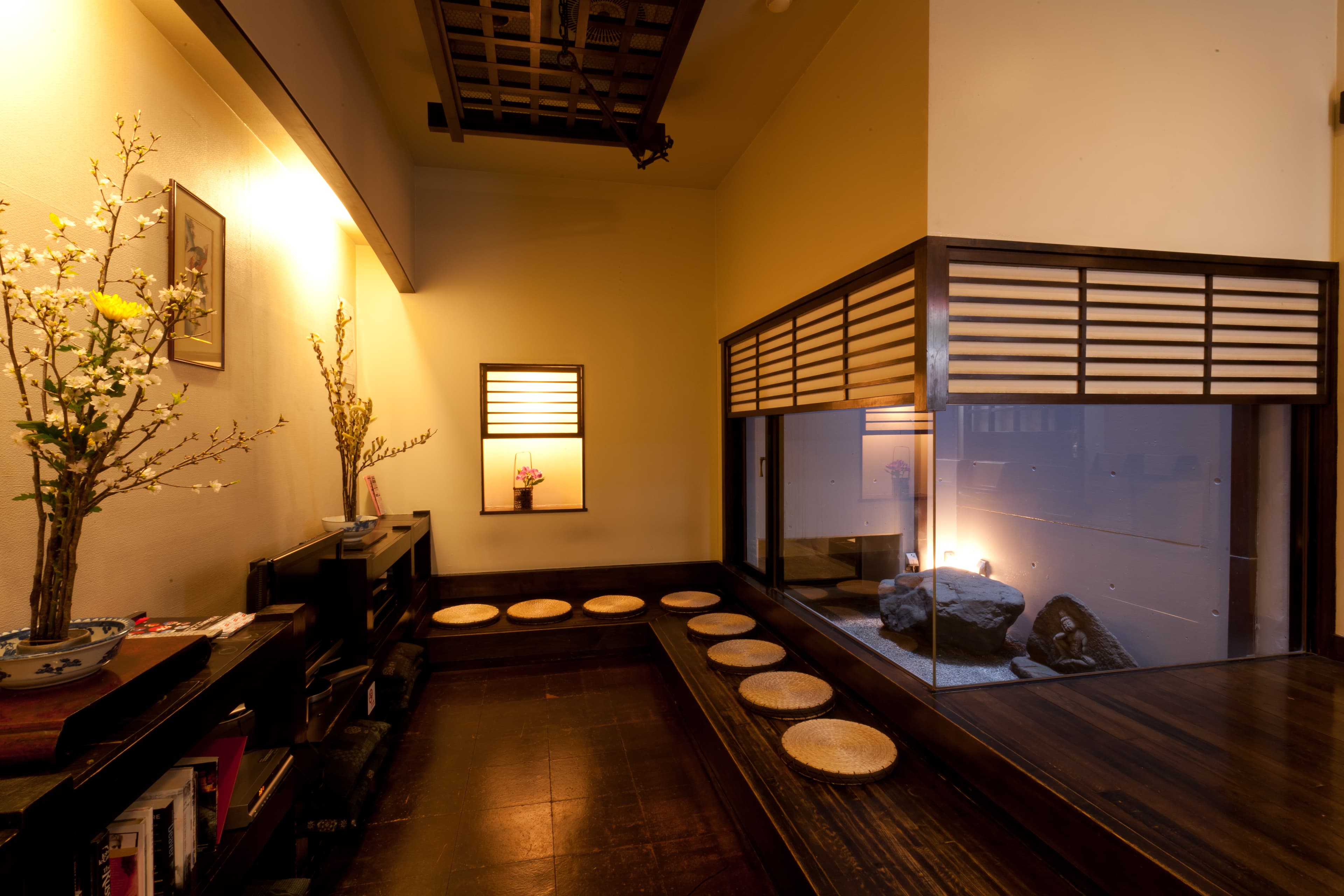 Kimi Ryokan lounge in Ikebukuro Tokyo with low wooden seating and a lit interior rock garden behind glass