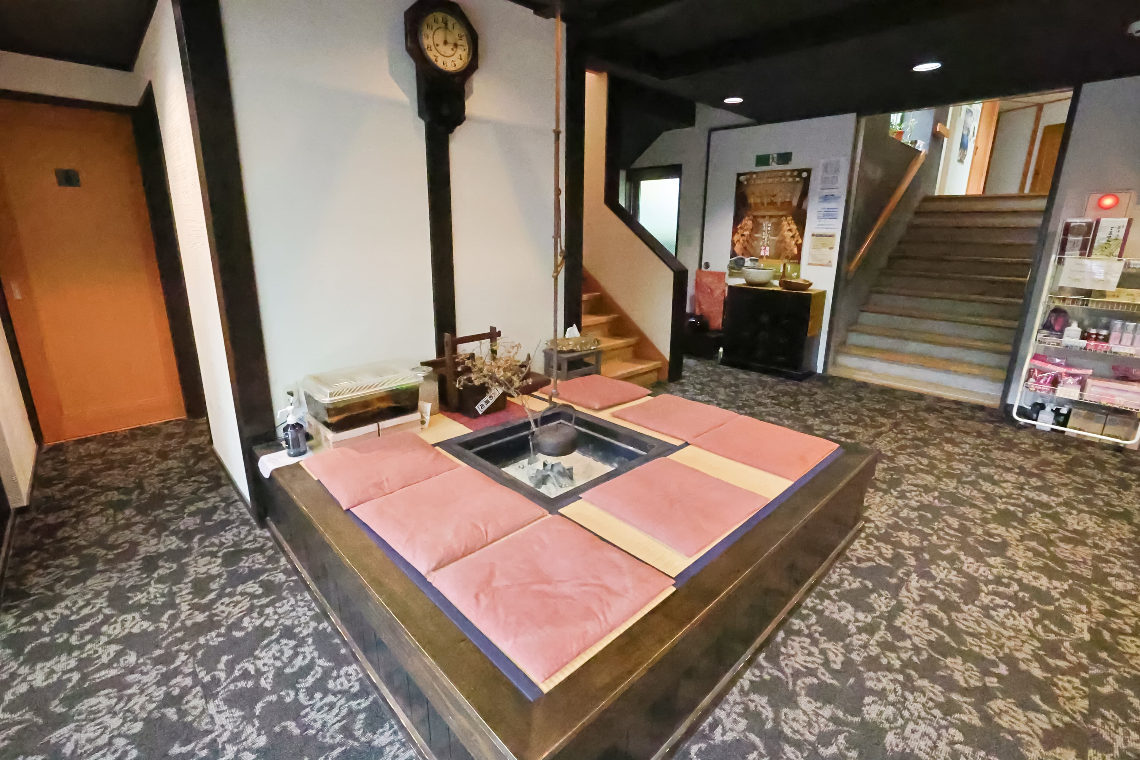 Lobby with a sunken irori hearth, pink floor cushions and an antique pendulum wall clock