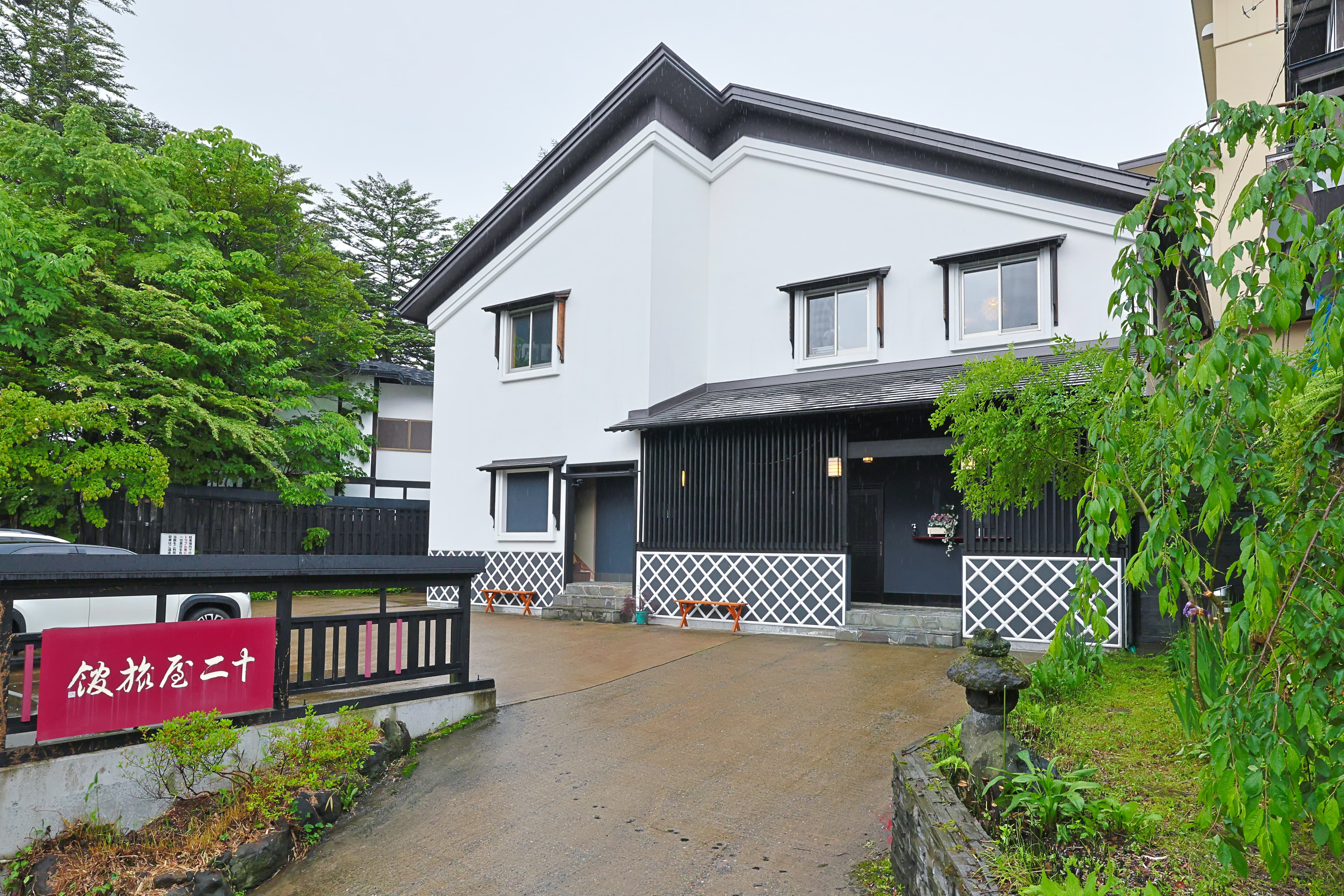 Juniya Ryokan exterior, a white kura-style building with dark slatted ground floor and a red name sign