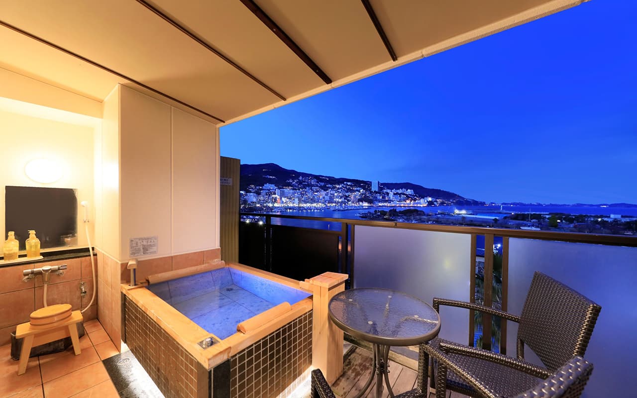 Guest room private open-air cypress bath with city and sea night view over Atami Onsen at Shukaen Yunohanazen