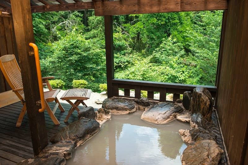 Private open-air stone bath with cloudy sulfur water overlooking the forest