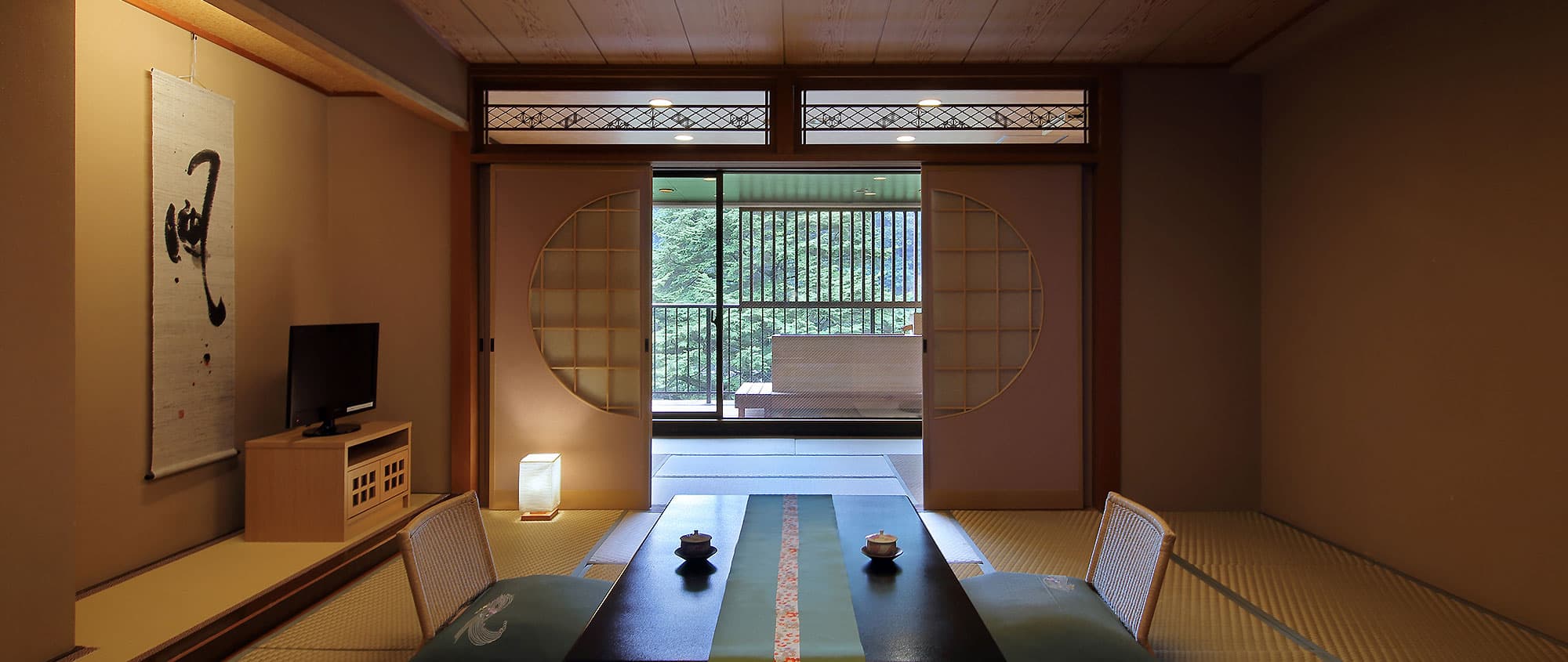 Tatami guest room at Hotel Tsuga no Ki with low table, hanging scroll and round shoji opening to a forest-view balcony