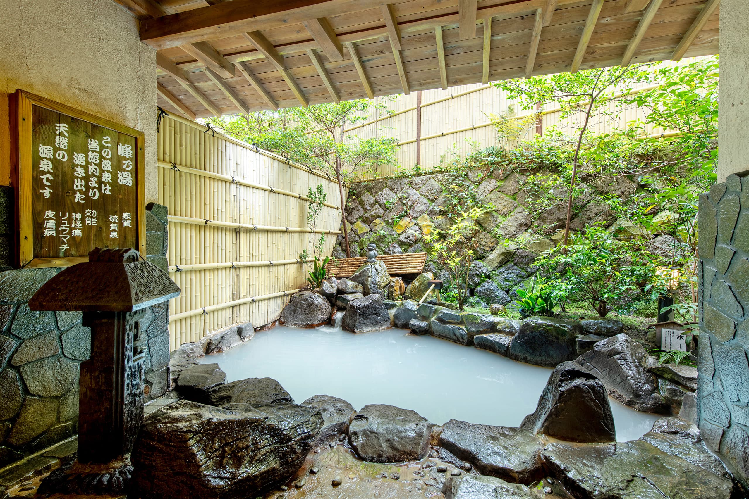 Open-air rotenburo with milky white sulphur hot spring water surrounded by rocks and a bamboo fence at Unzen Iwaki Ryokan