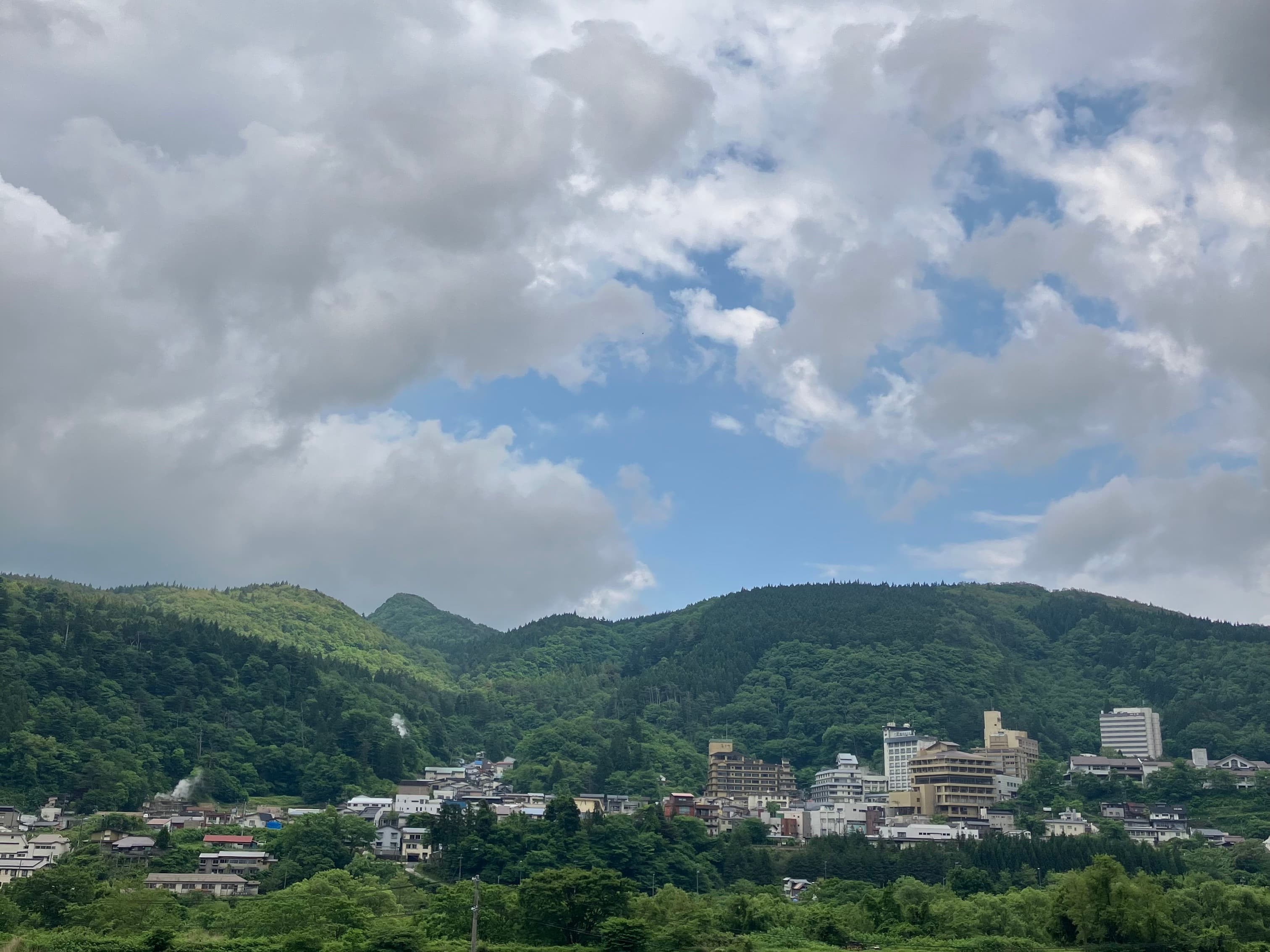 Naruko Onsen town with steam rising from hot springs, forested mountains in background, Miyagi — photo by Zhaitengli, CC BY 4.0