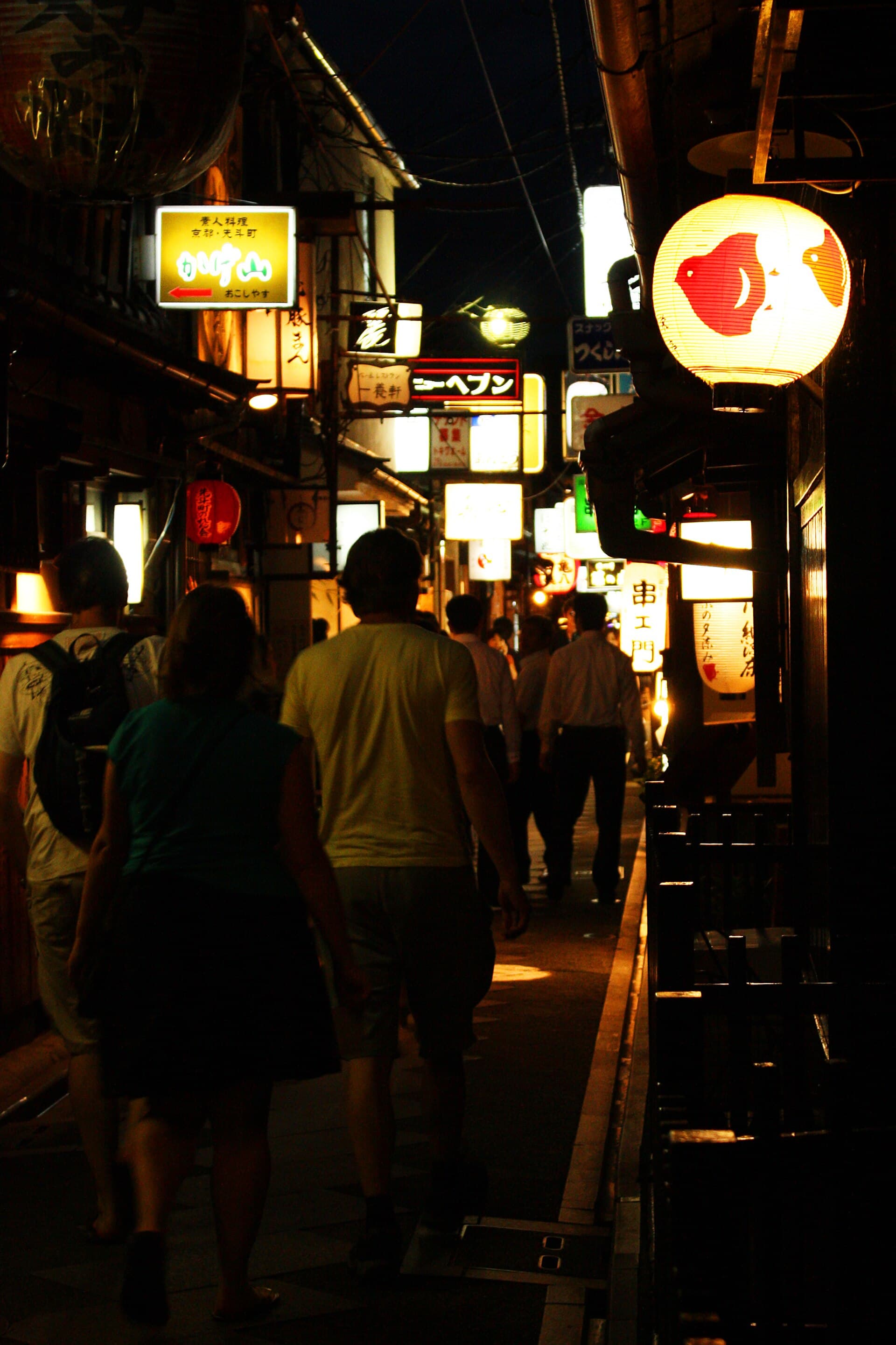 Single person walking a narrow traditional Japanese street lined with wooden merchant buildings at dusk in Kyoto, evoking solo evening freedom in Japan's historic towns