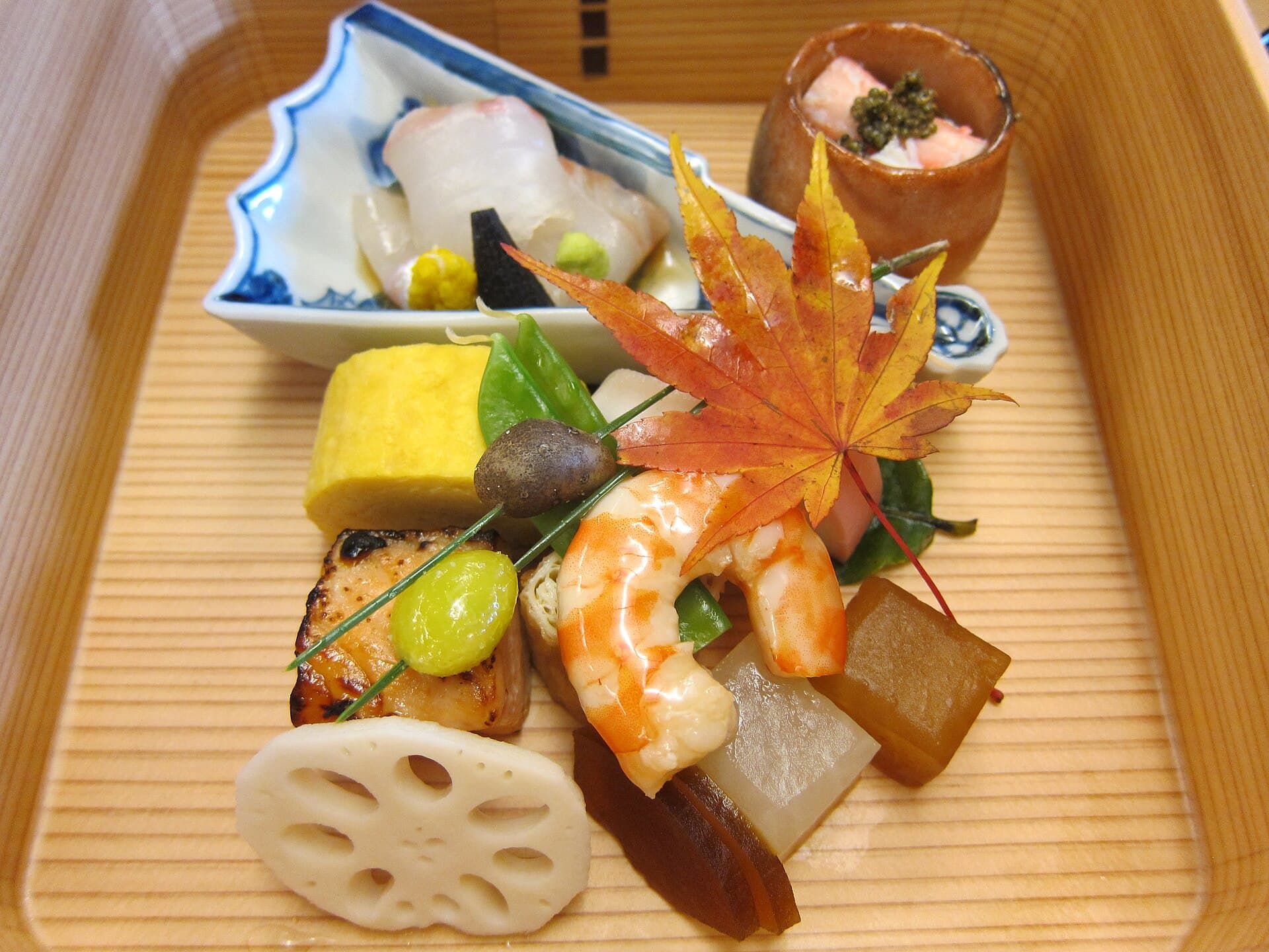 Multiple small ceramic bowls in red and green lacquerware arranged on a dark wooden tray, Japanese multi-course meal presentation