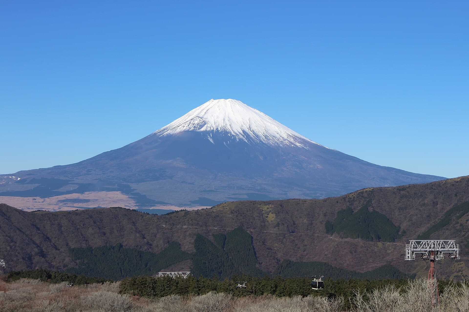 View of the steaming volcanic vents of Owakudani valley in Hakone, with Mt. Fuji visible in the distant background on a clear day.