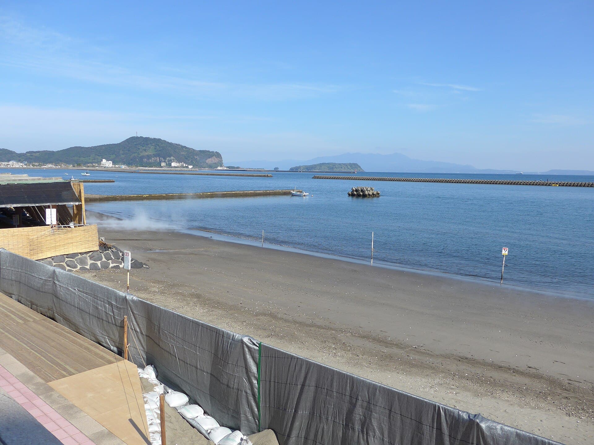 Travelers buried up to their necks in the dark sand of the Ibusuki sand baths, with colorful parasols providing shade.